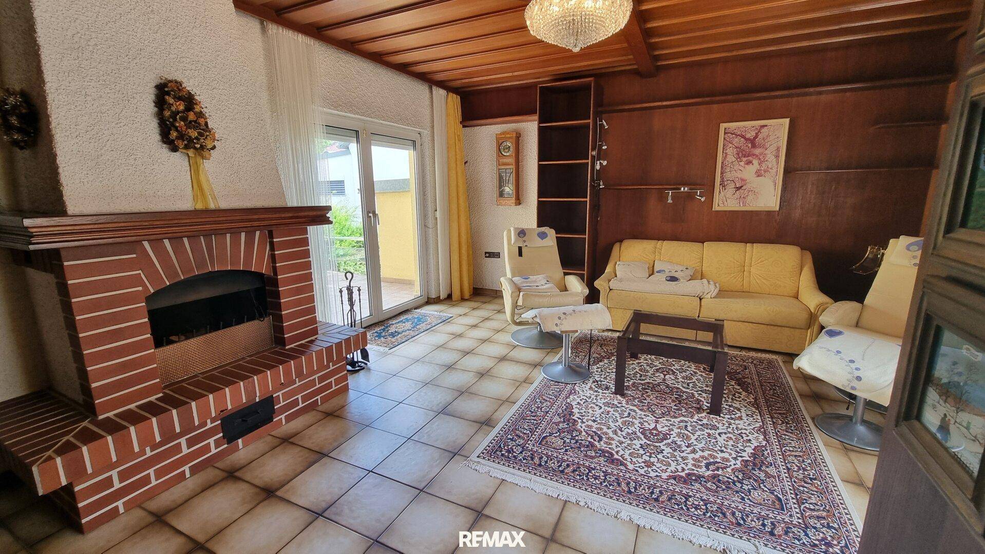 Gemütliches Wohnzimmer mit Kamin, Fliesenboden und Holzvertäfelung im Landhausstil.