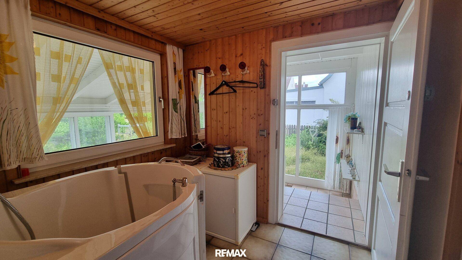 Badezimmer mit Badewanne, Holzvertäfelung und Fenster mit Blick ins Grüne.