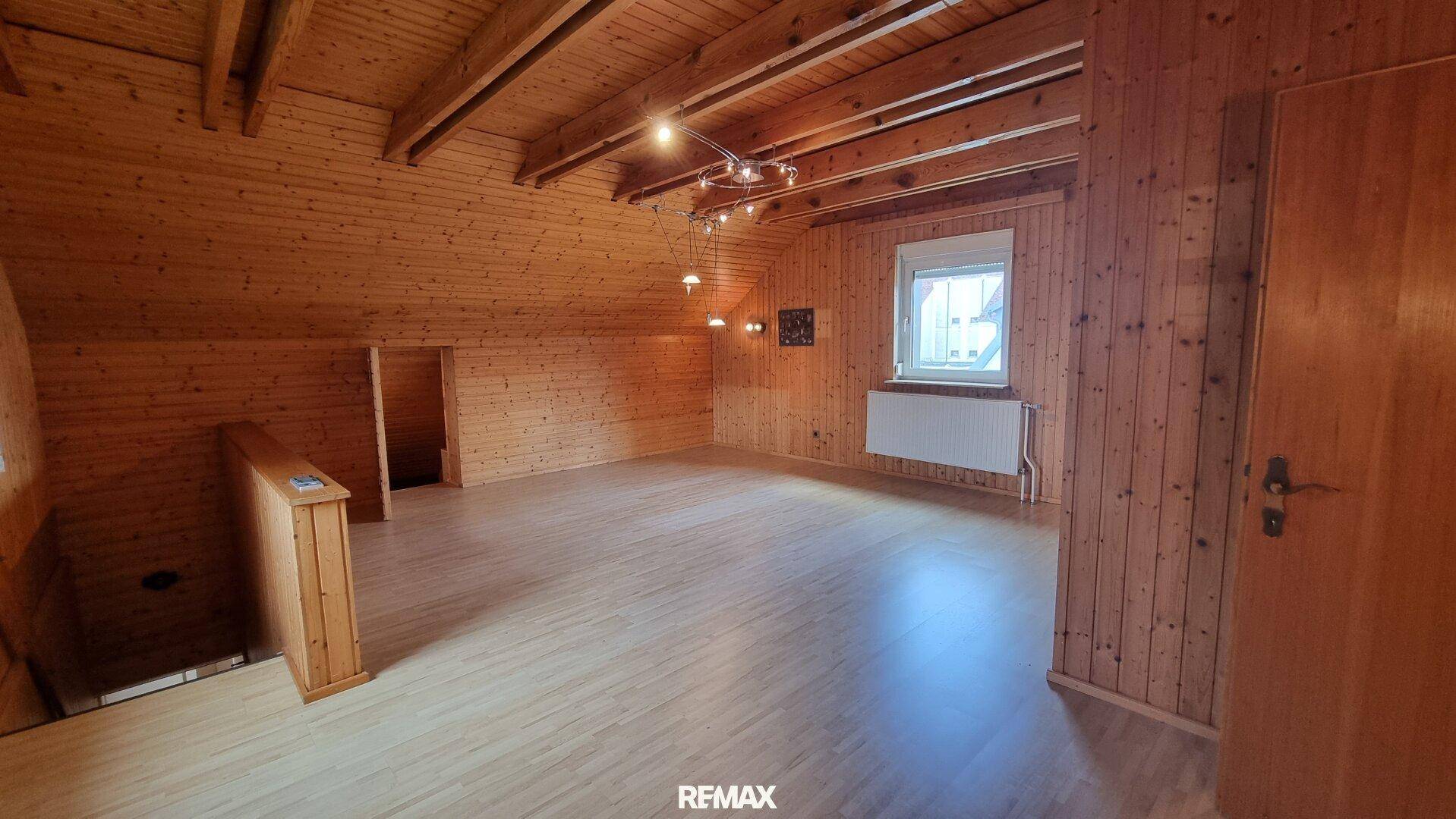 Geräumiges Dachzimmer mit Holzvertäfelung, Laminatboden und Dachschrägen.
