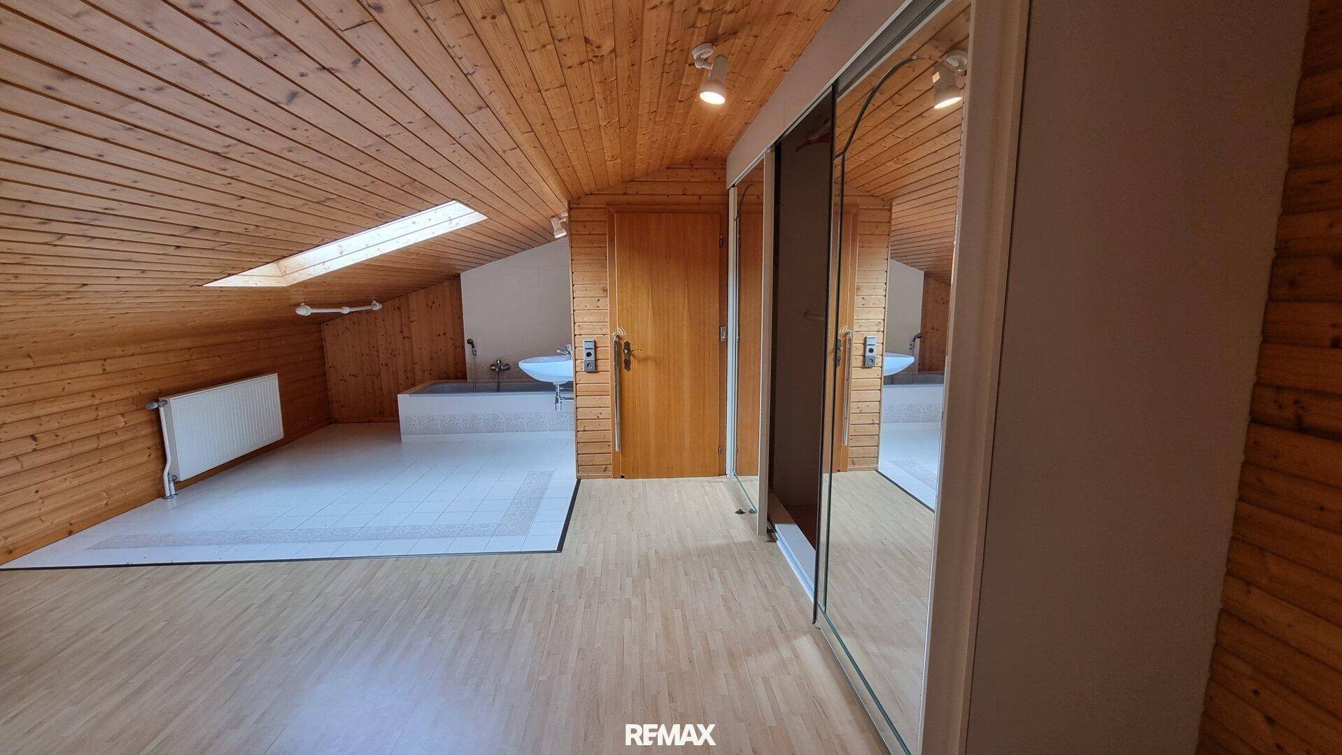 Dachzimmer mit Holzvertäfelung, Laminatboden und einem Bereich mit Waschbecken.