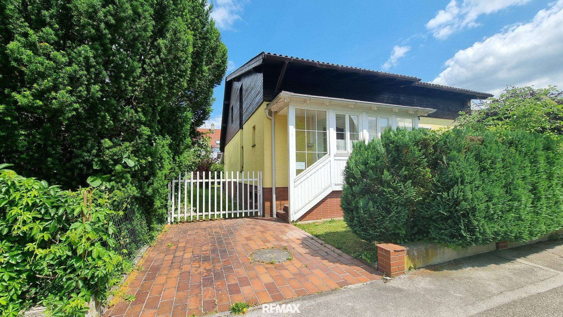 Einfahrt zum Haus mit weißem Zaun, Hecken und gepflastertem Bereich.