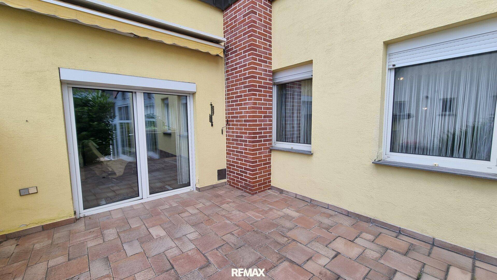 Gepflasterte Terrasse an der Hauswand mit Zugang zum Wintergarten.