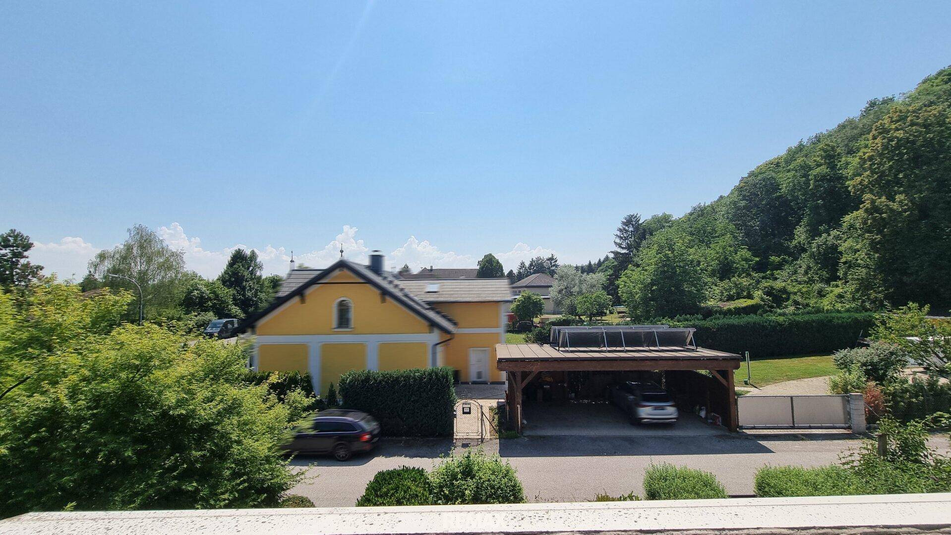 Weitblick über die Nachbarschaft mit einem gelben Haus und einem Carport unter blauem Himmel.