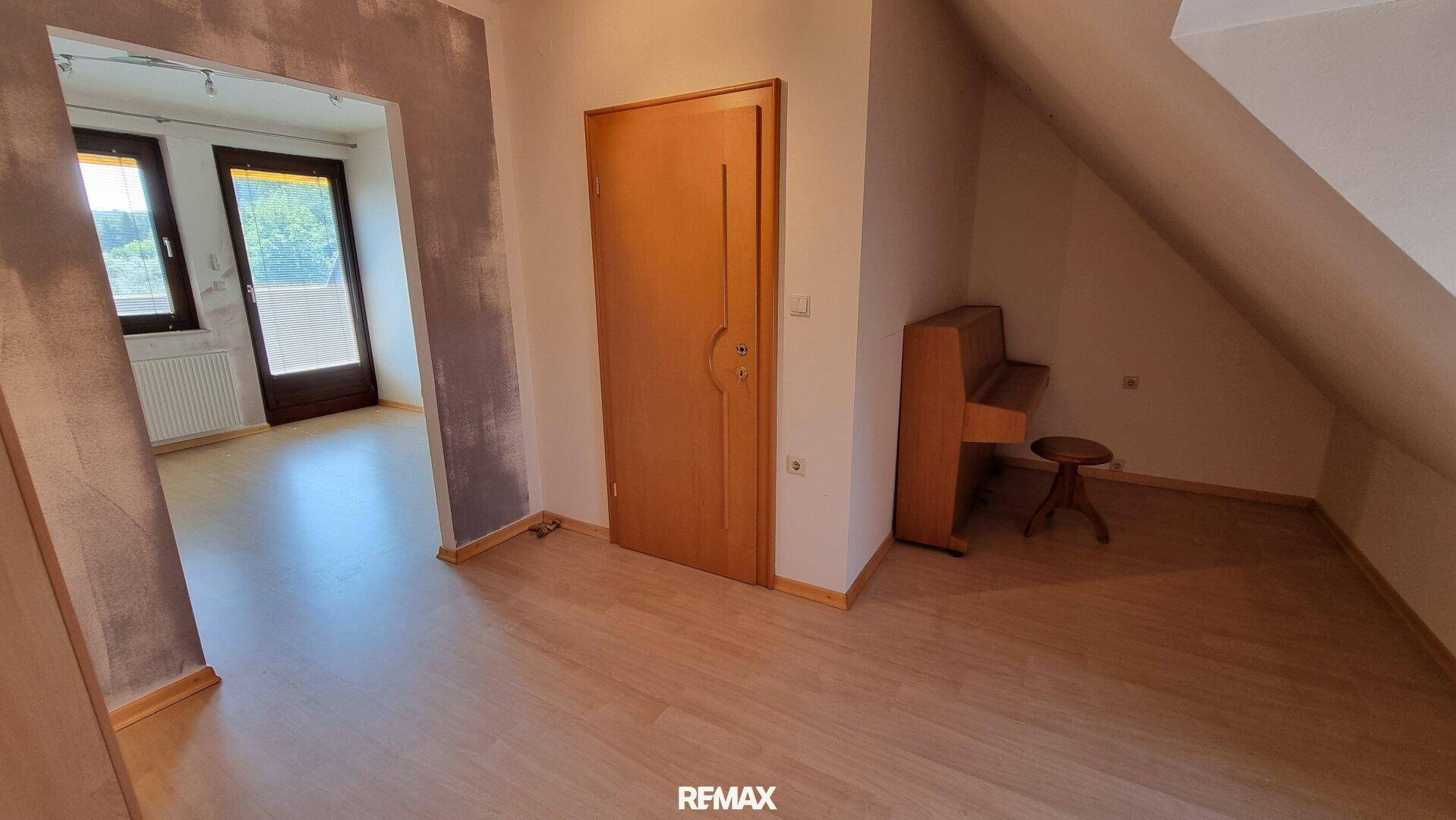 Dachgeschosszimmer mit schräger Decke, Laminatboden und einem Klavier, bietet viel Potenzial.