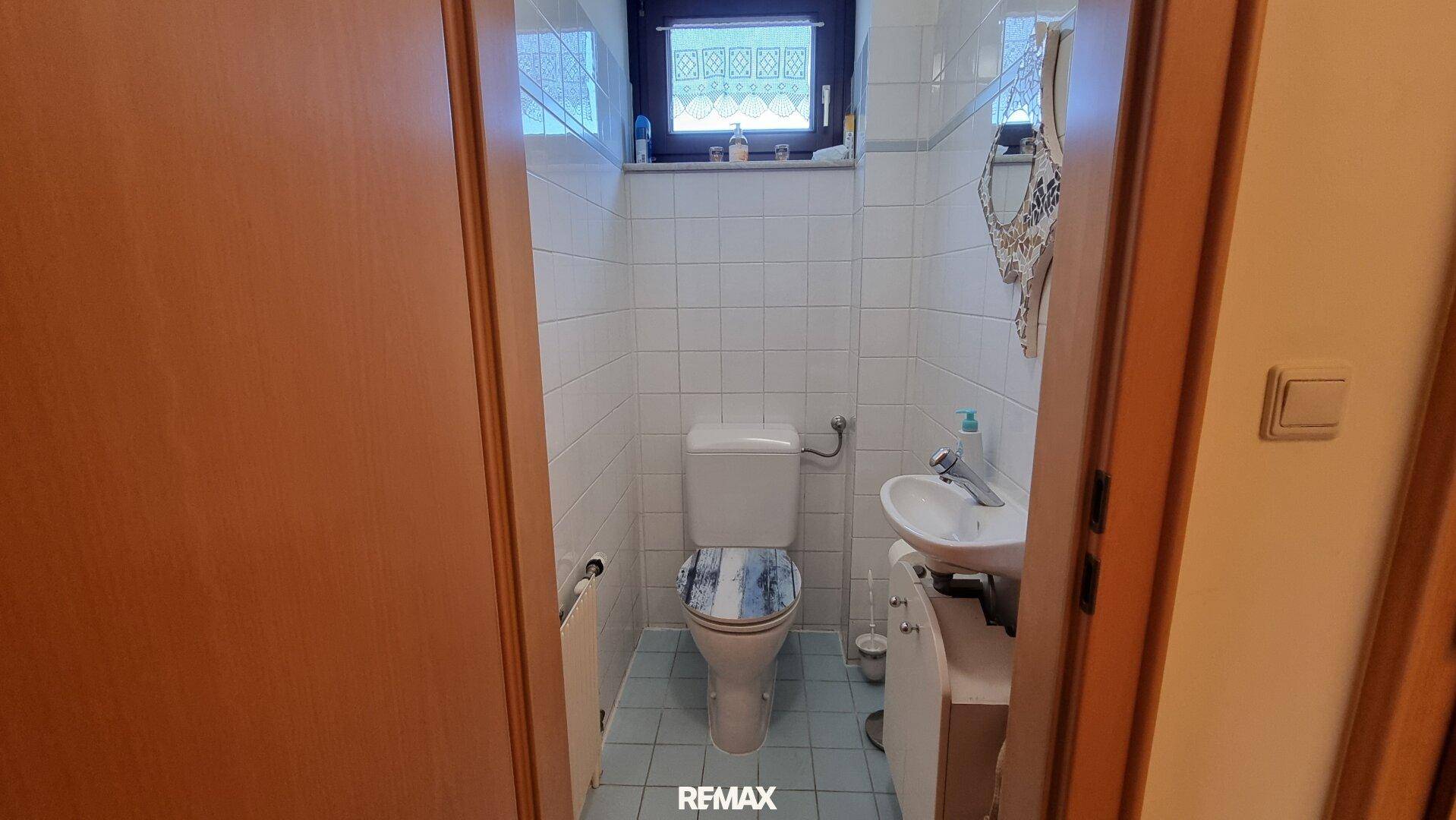 Kleines Gäste-WC mit Fenster, hellblauen Fliesen und einfacher, funktionaler Ausstattung.