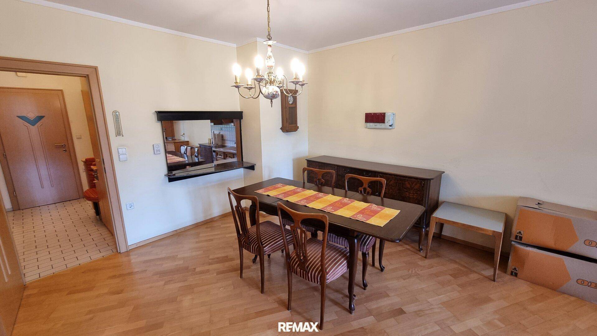 Esszimmer mit Holztisch, passenden Stühlen, einem eleganten Kronleuchter und Parkettboden.