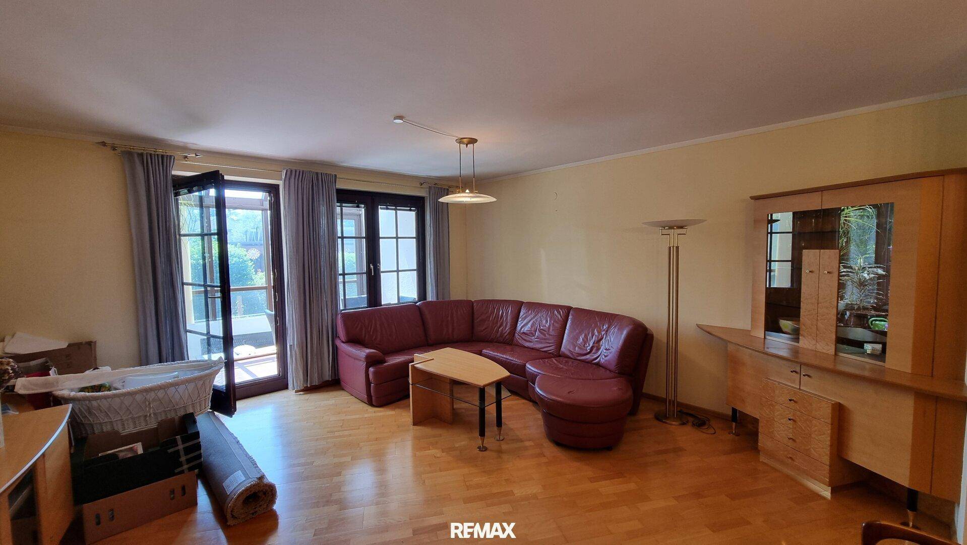 Geräumiges Wohnzimmer mit rotem Ledersofa, Parkettboden und Zugang zu einem Balkon.