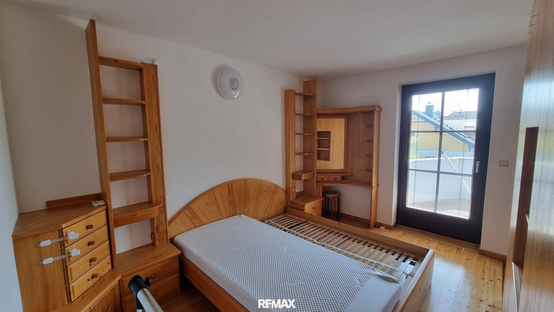 Schlafzimmer mit Holzbettenrahmen, integrierten Regalen und Zugang zu einem kleinen Balkon.