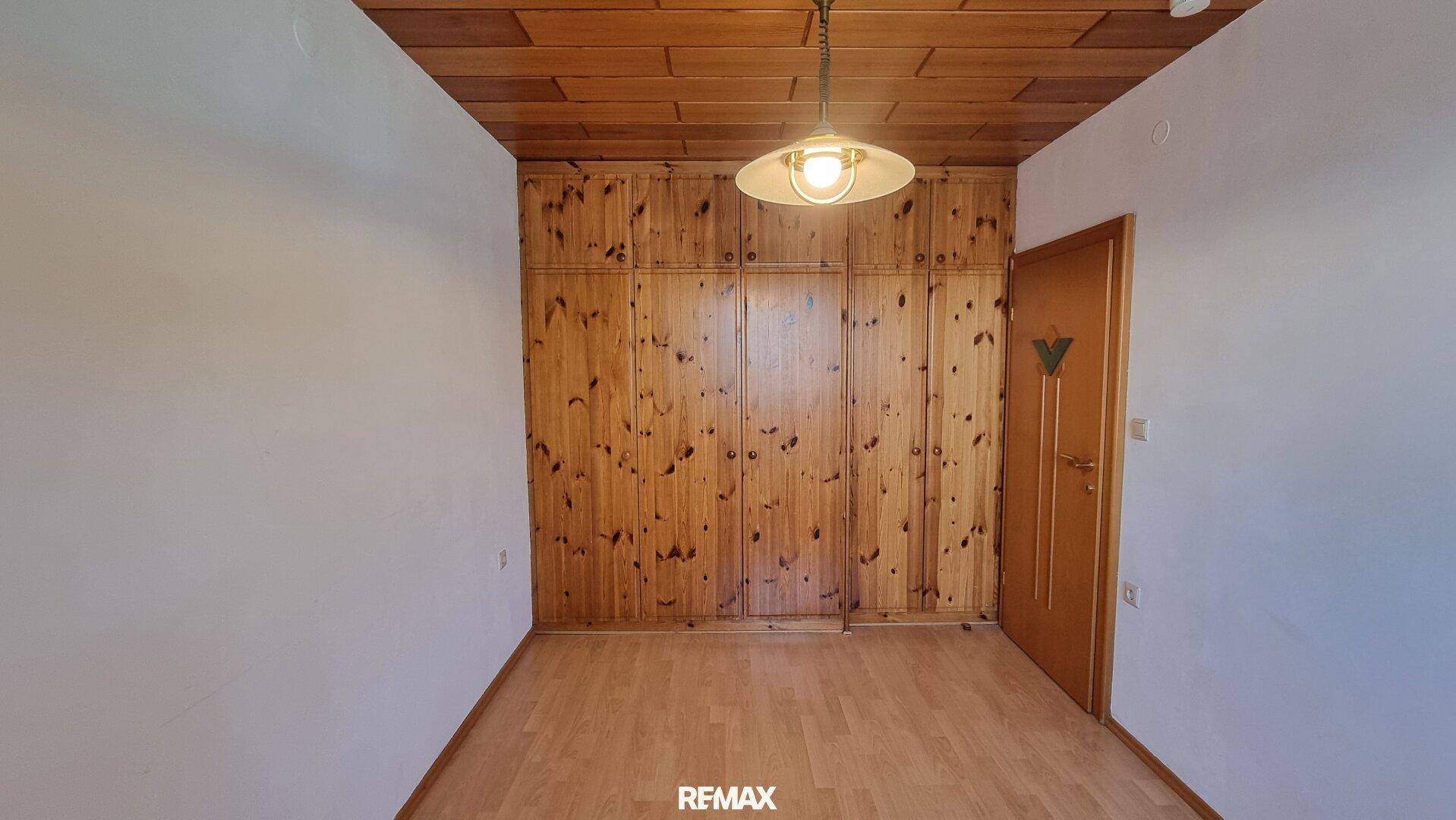 Schlafzimmer mit Holzwand, großem Einbauschrank und Parkettboden, strahlt Gemütlichkeit aus.