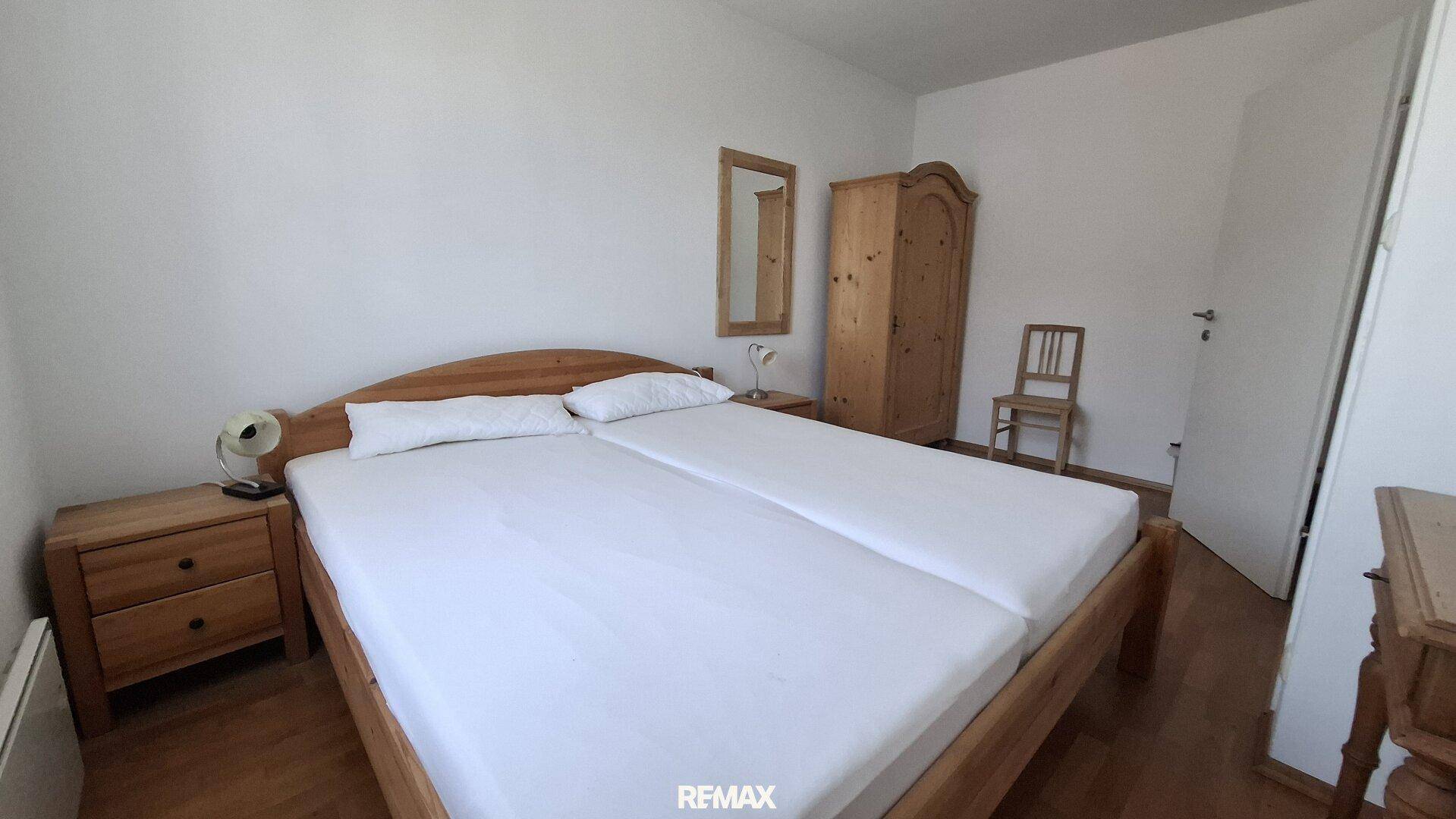 Helles Schlafzimmer mit zwei Einzelbetten, Holzmöbeln und Parkettboden.