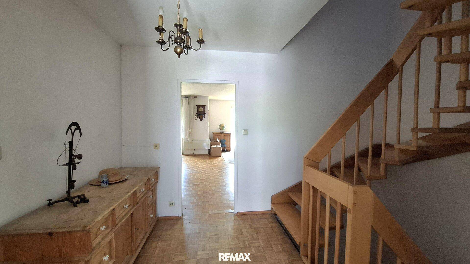 Heller Flur mit Holztreppe, Parkettboden und traditioneller Kommode.
