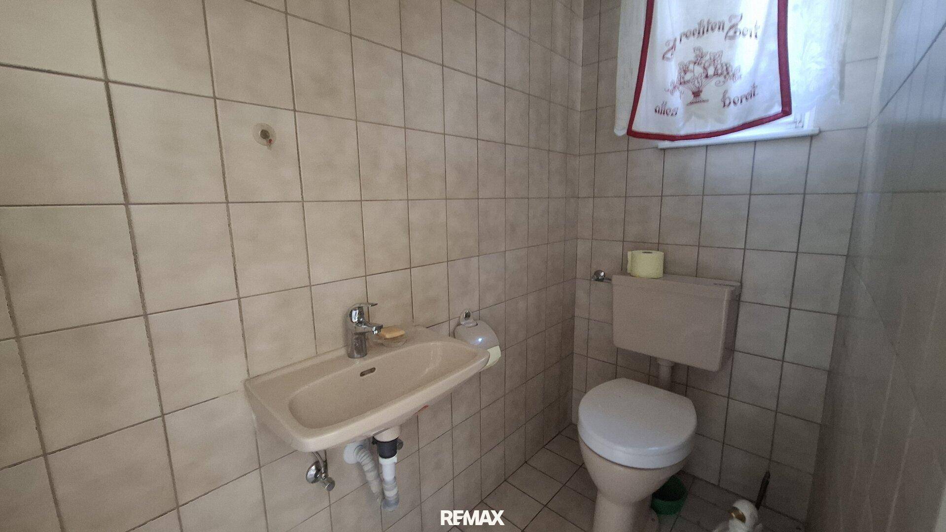 Kleines Gäste-WC mit beigen Fliesen, Waschbecken und Toilette.