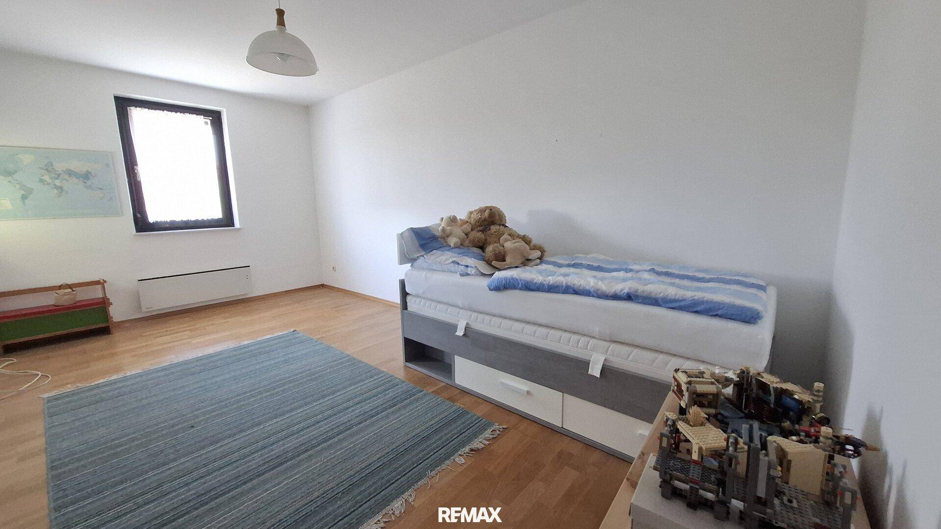 Kinderzimmer mit Einzelbett, Parkettboden und großem Fenster für viel Tageslicht.