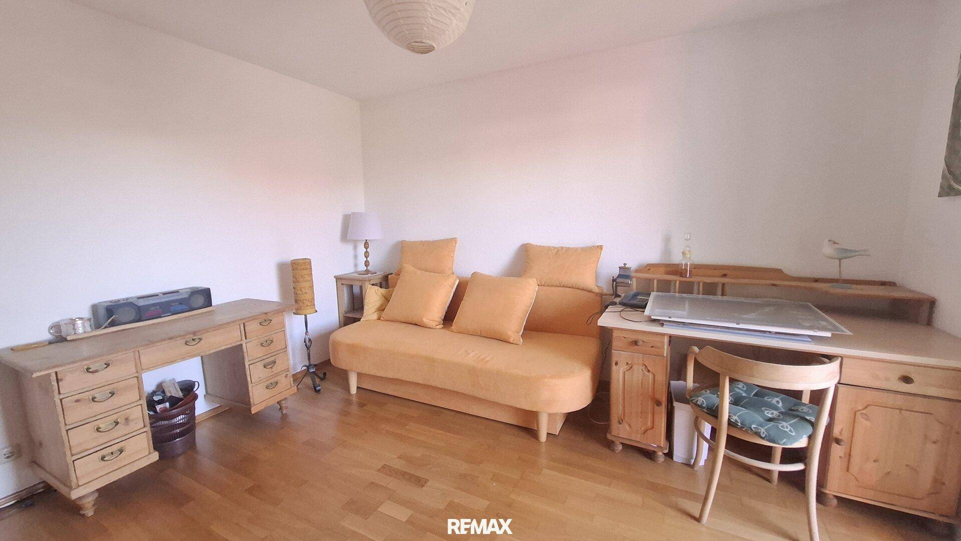 Arbeitszimmer mit Holzschreibtischen, Sofa und Parkettboden.