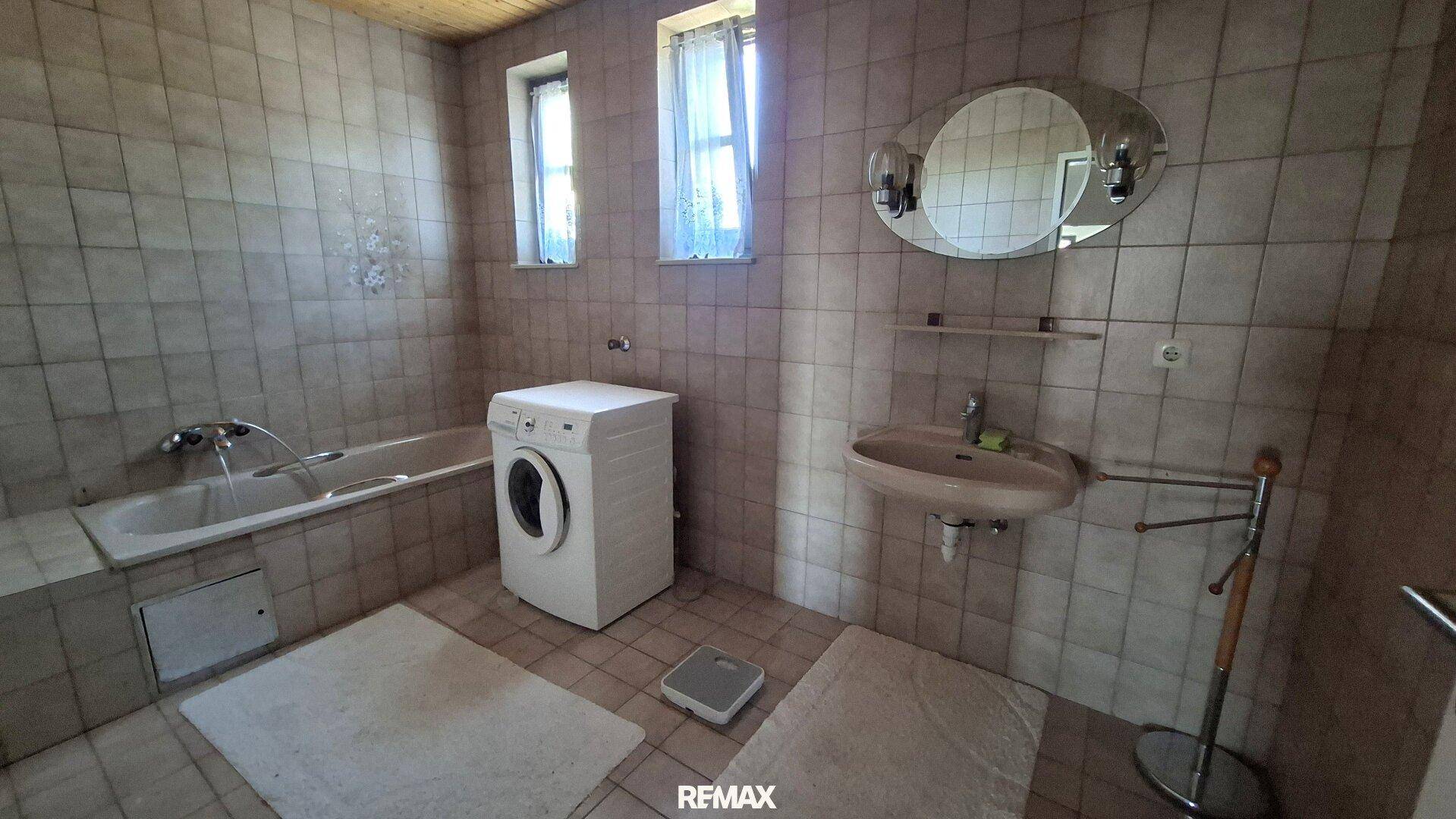 Badezimmer mit Badewanne, Waschmaschine, Waschbecken und Fenster.