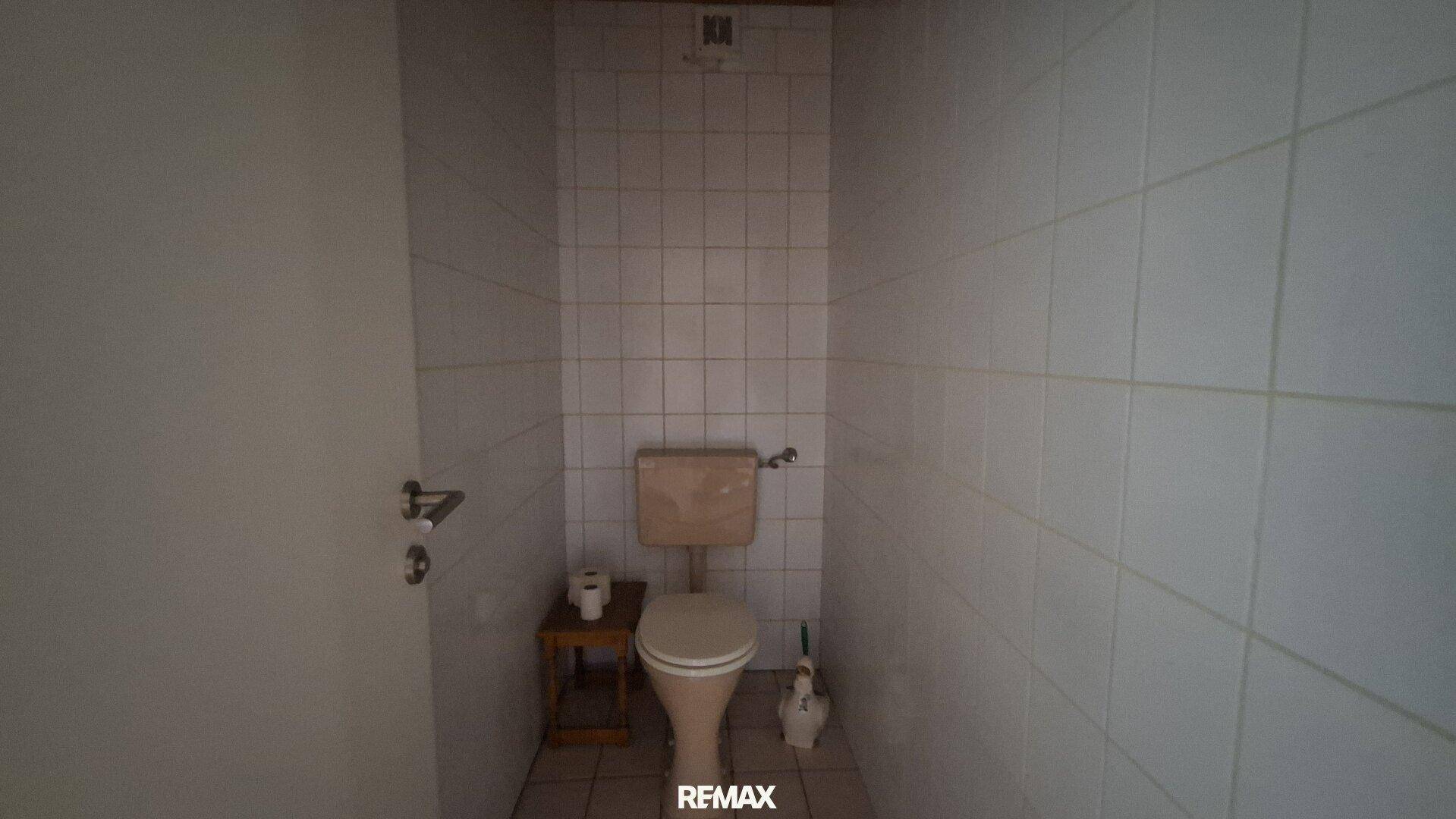 Separates WC mit weißen Fliesen und einfacher Toilette.