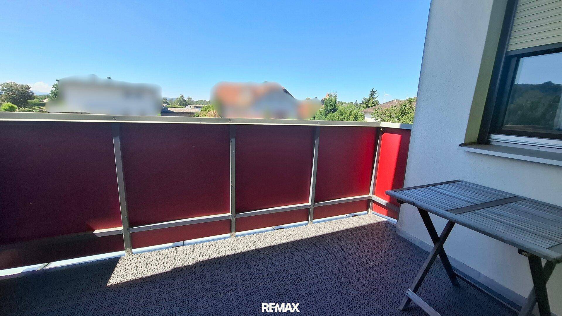 Kleiner Balkon mit roter Verkleidung und Tisch, ideal für eine Kaffeepause.