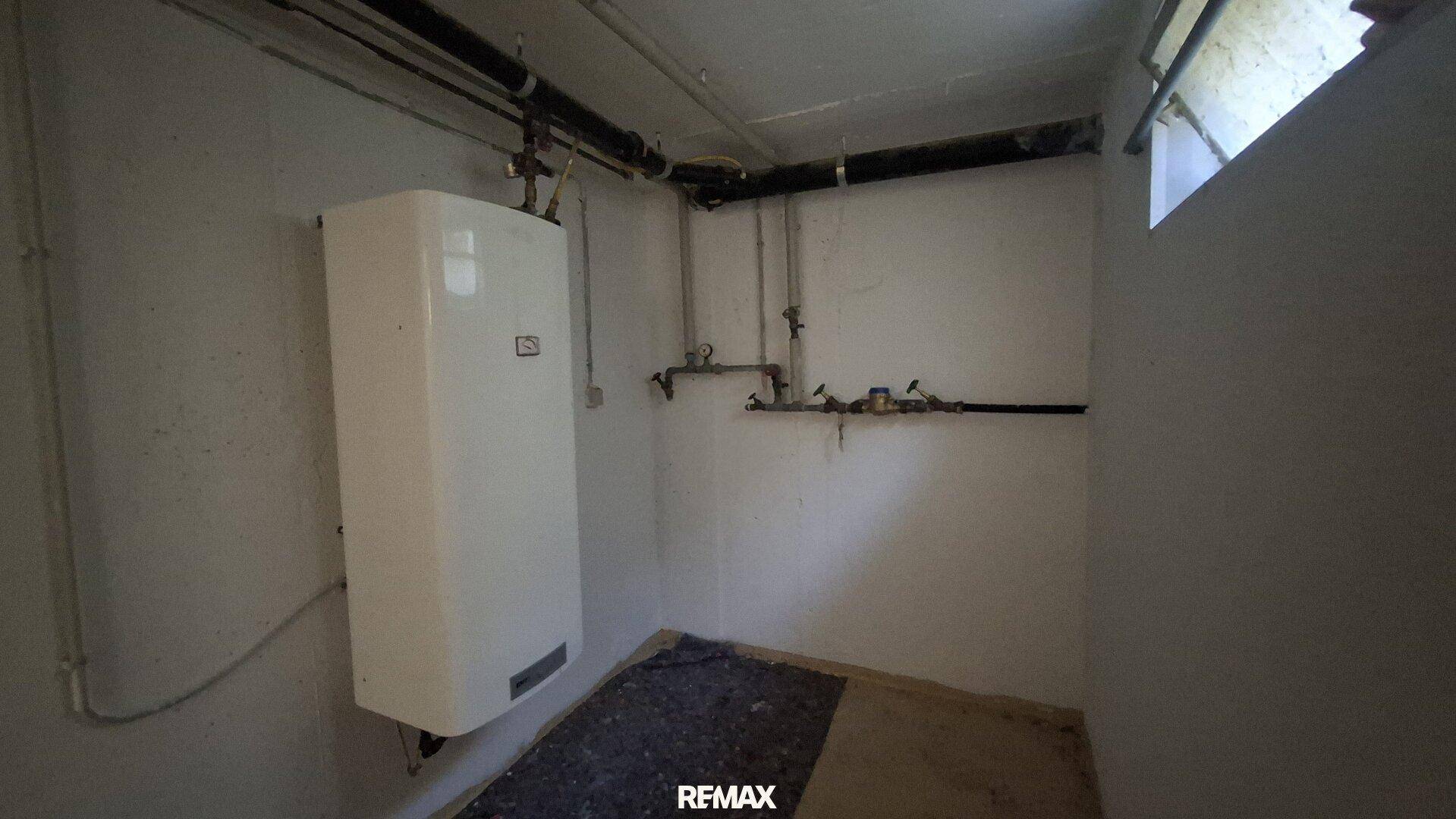 Heizungsraum im Keller mit Warmwasserboiler und sichtbaren Rohren.