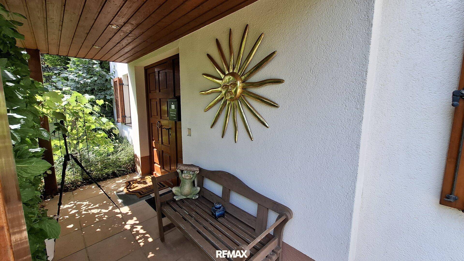 Überdachter Eingangsbereich mit Holztür und dekorativer Sonnenskulptur.