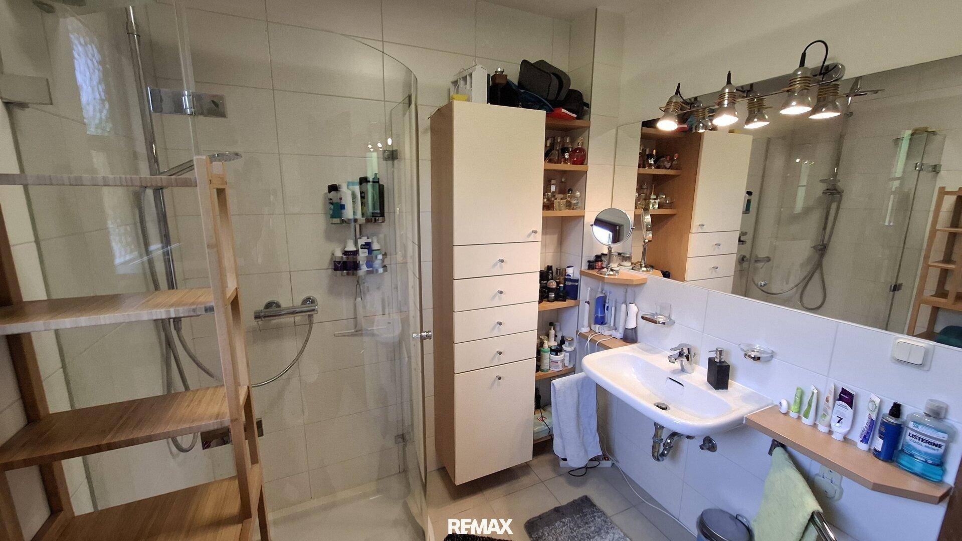 Modernes Badezimmer mit Duschkabine, großem Spiegel und Einzelwaschbecken.