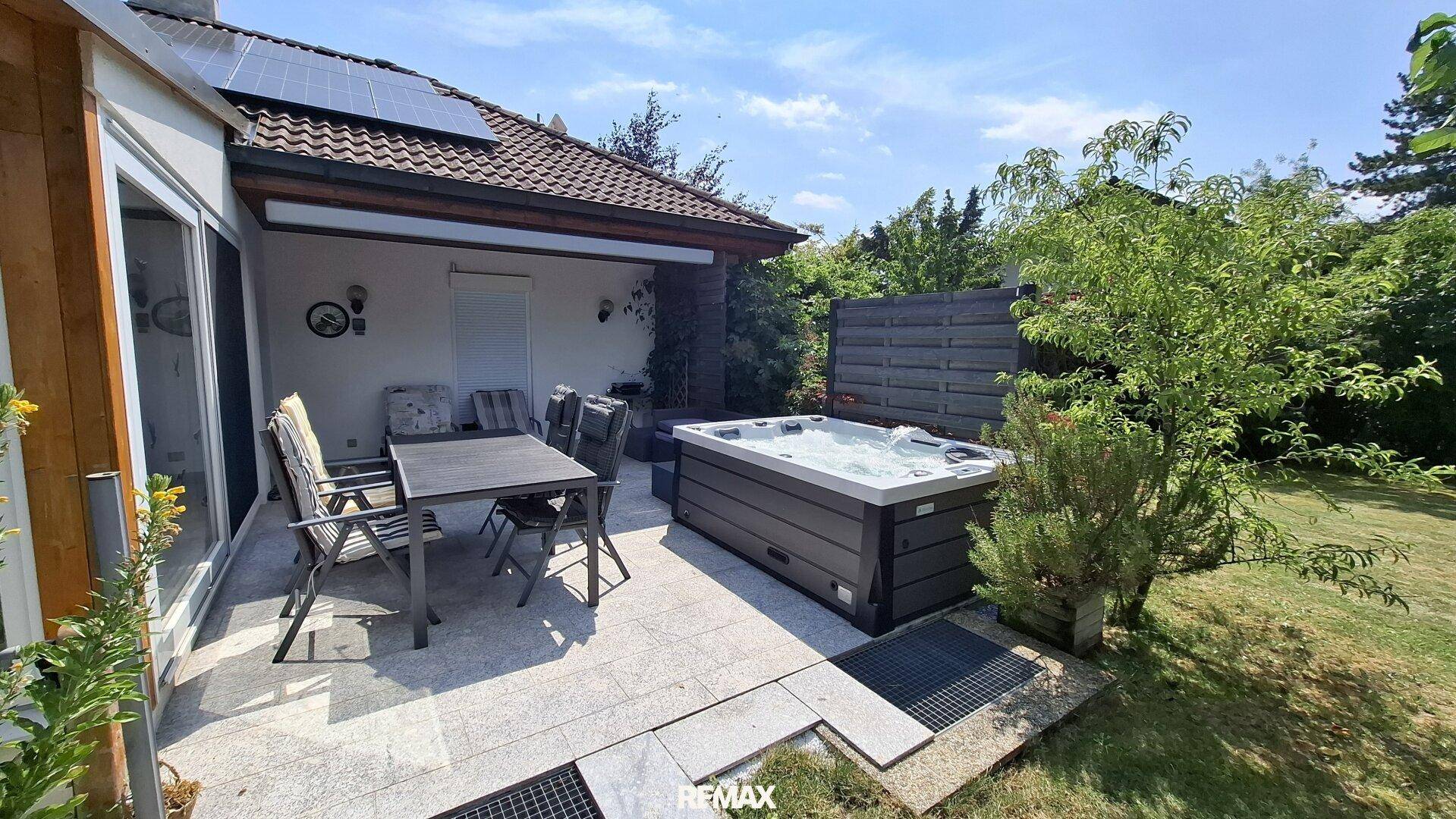 Sonniger Terrassenbereich mit Whirlpool und Essbereich, umgeben von viel Grün.