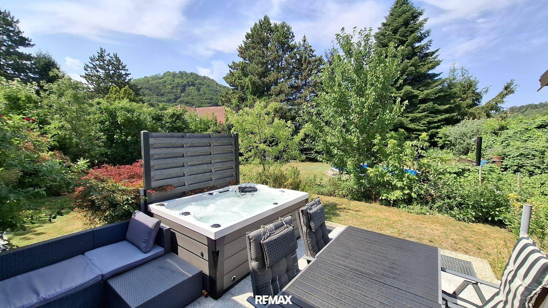 Gemütlicher Terrassenbereich mit Outdoor-Sofa und Whirlpool, umgeben von Natur.