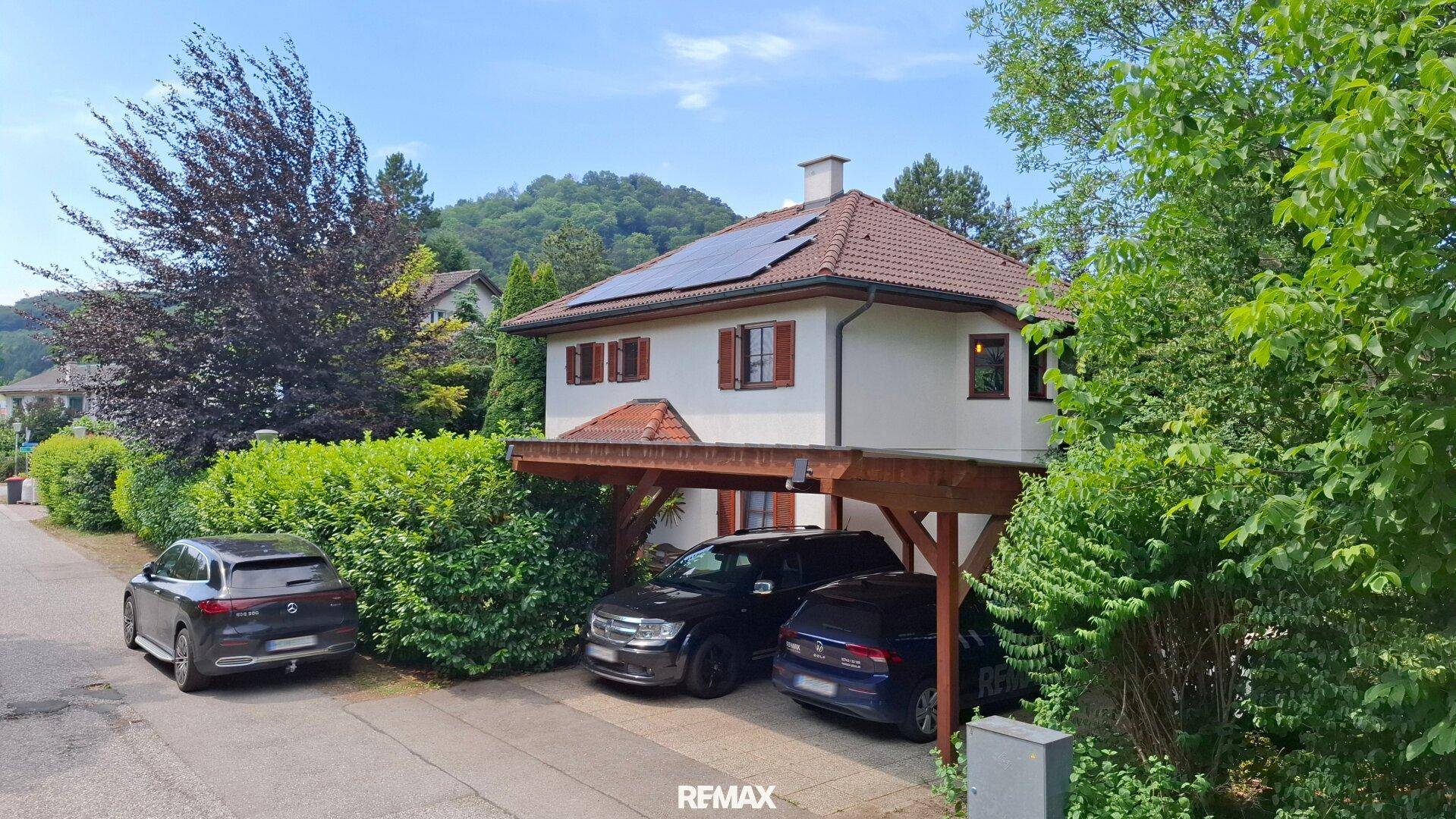Einfamilienhaus mit Carport und Photovoltaikanlage, umgeben von gepflegter Hecke.