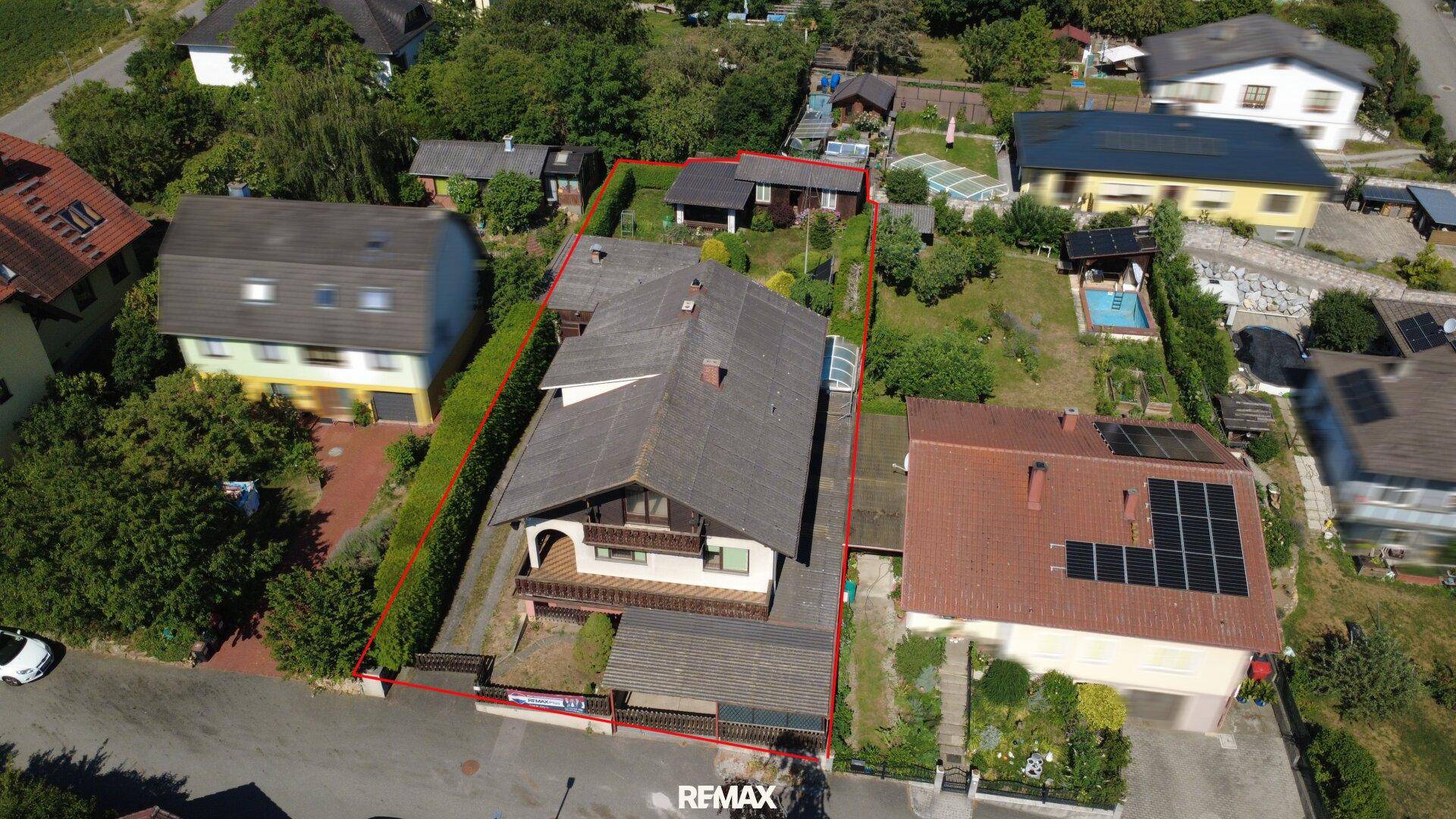 Luftaufnahme des Anwesens mit Haus, Garten und umliegender Wohnbebauung unter blauem Himmel.