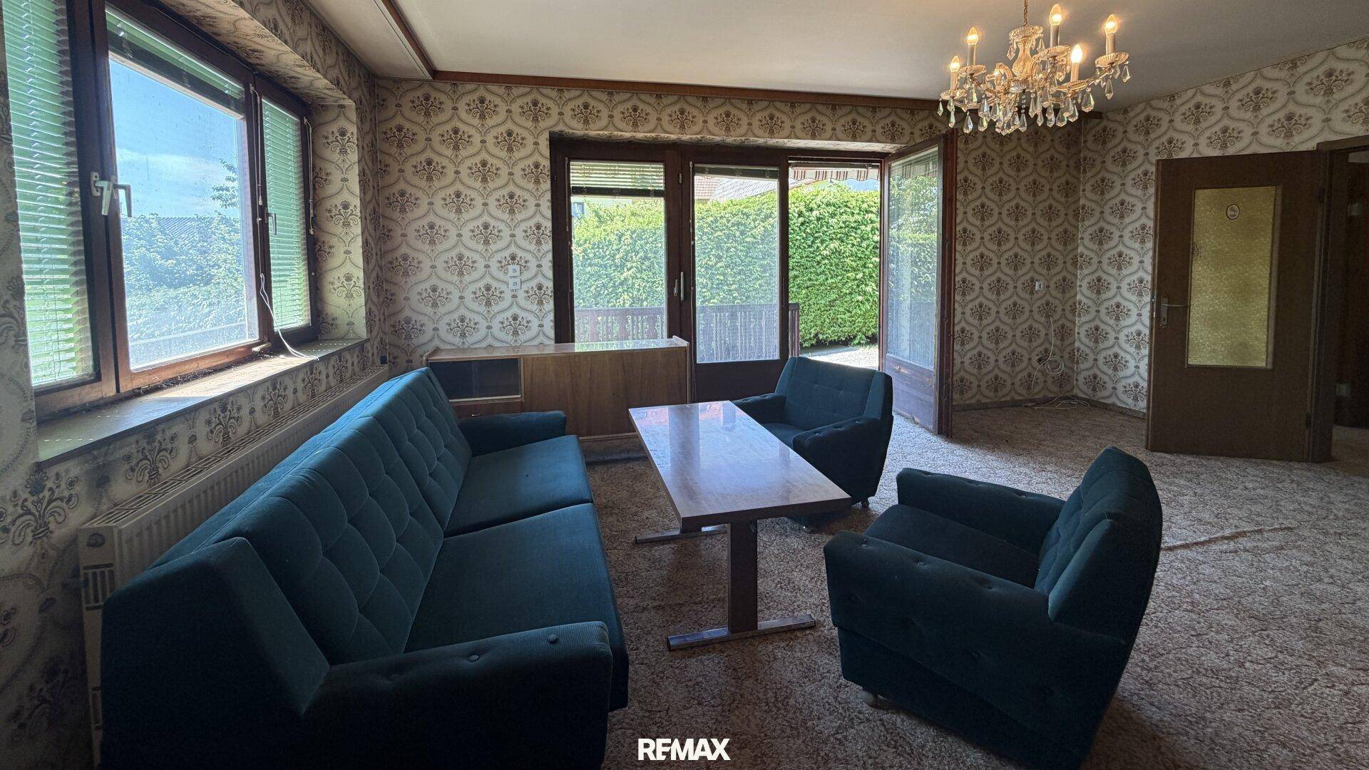 Wohnzimmer im Vintage-Stil mit gemusterter Tapete, Teppichboden und Zugang zu einem Außenbereich.