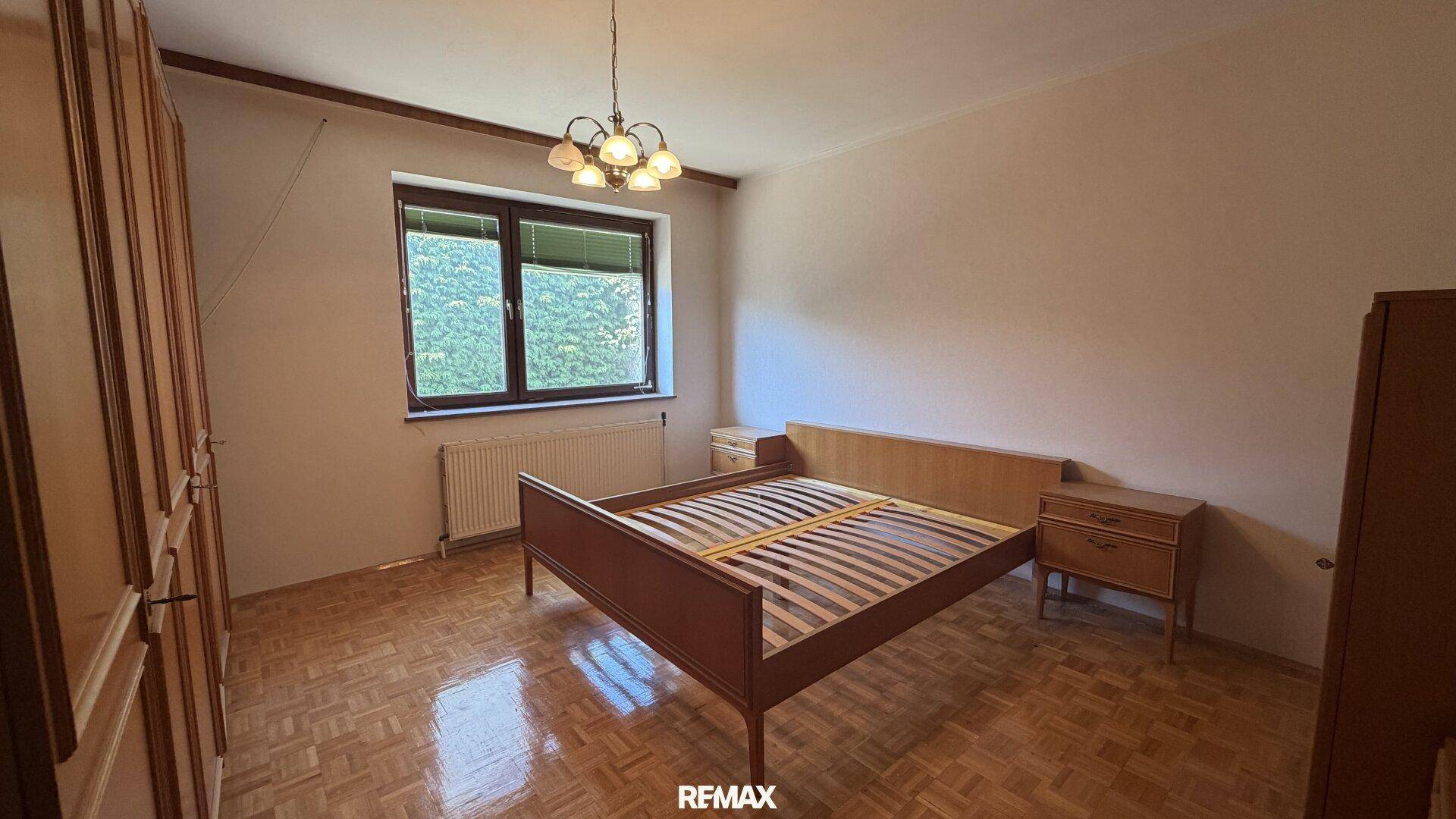 Helles Schlafzimmer mit Parkettboden, einem Doppelbett und einem Fenster mit Blick ins Grüne.