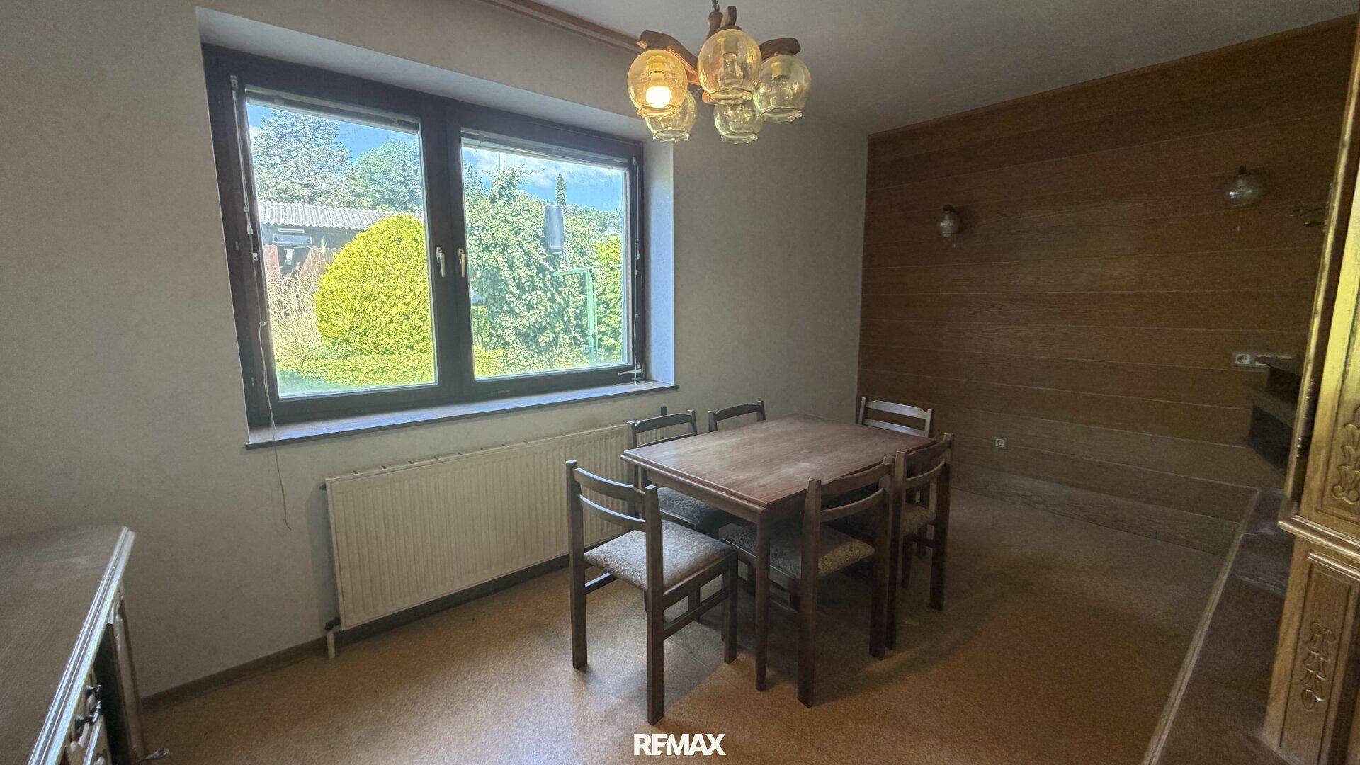 Esszimmer mit Holztisch und Stühlen, Holzvertäfelung an der Wand und Blick in den Garten.