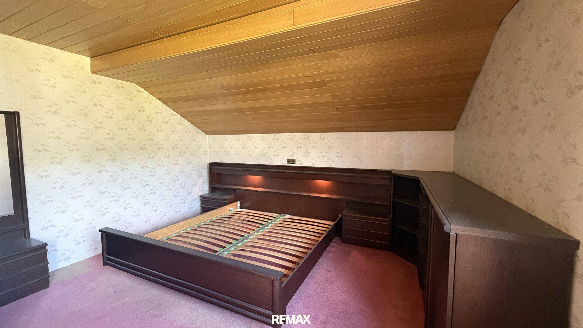 Dachschlafzimmer mit schräger Holzdecke und dunklen Einbaumöbeln, die den Raum optimal nutzen.