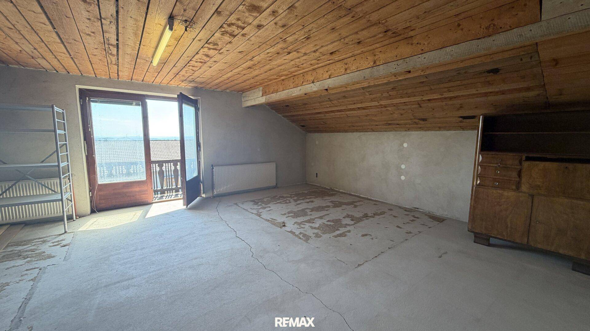 Geräumiger Dachbodenraum mit Betonboden, Holzdecke und Zugang zu einem Balkon, ideal für Ausbau.