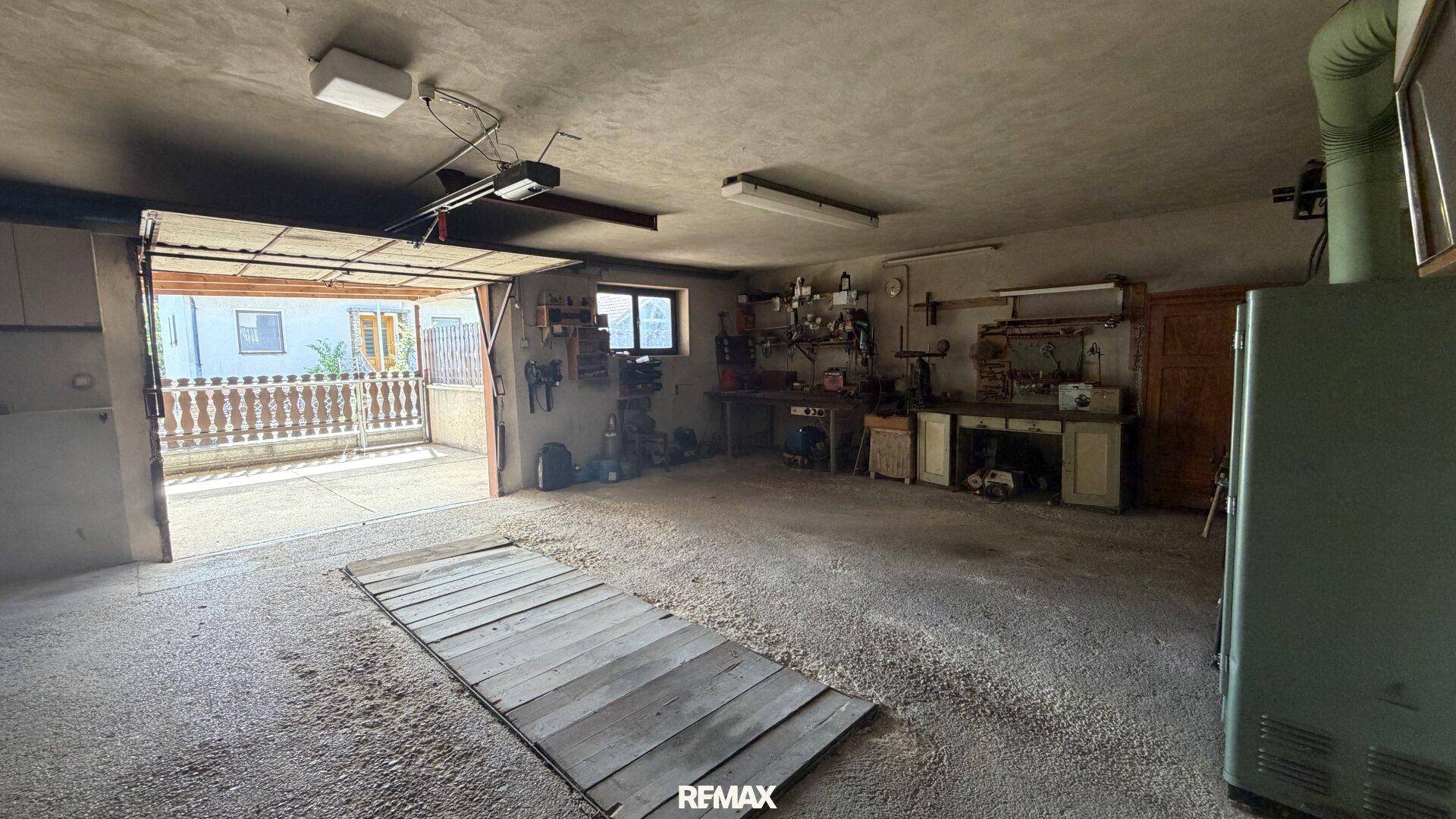 Geräumige Garage oder Werkstatt mit offenem Tor, Werkbänken und viel Platz für Fahrzeuge und Hobbys.