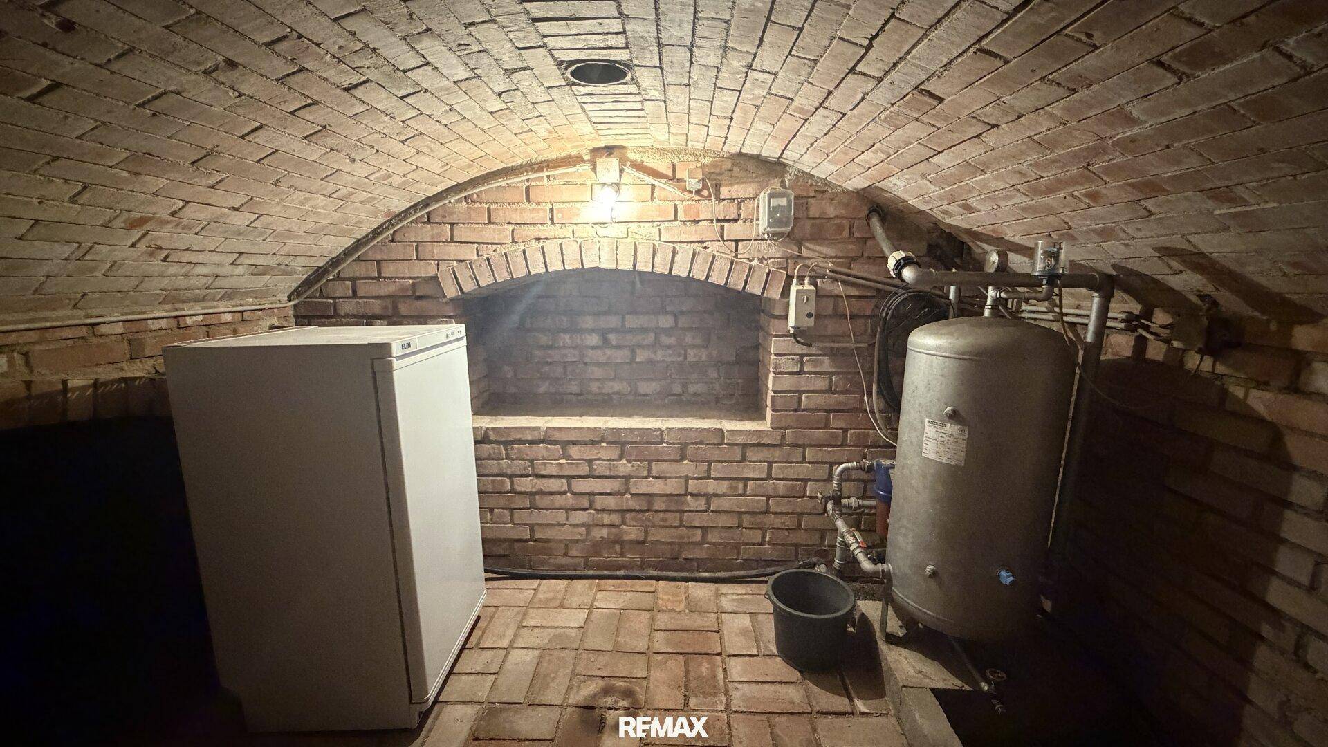 Gewölbekeller aus Ziegelstein mit einem Warmwasserspeicher und einem Kühlschrank, ideal für Lagerung.