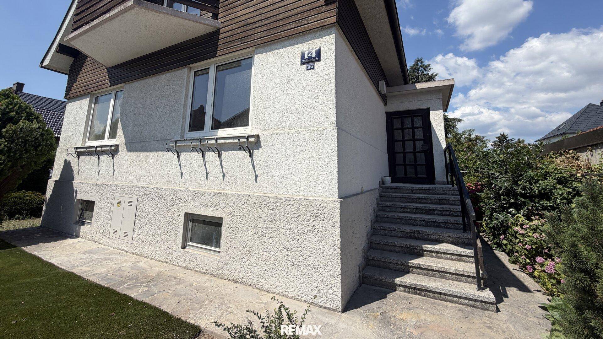 Seitenansicht des Hauses mit Außentreppe zum Eingang und kleinen Fenstern im Untergeschoss.