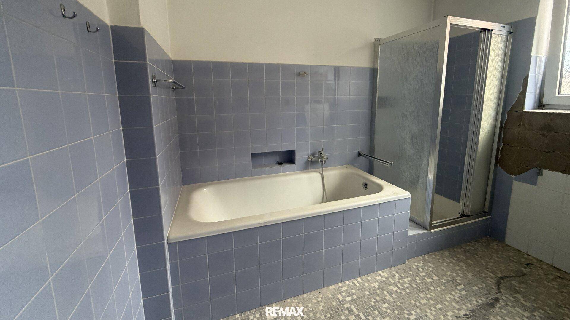 Badezimmer im Stil der 80er Jahre mit blauen Fliesen, Badewanne und Duschkabine.