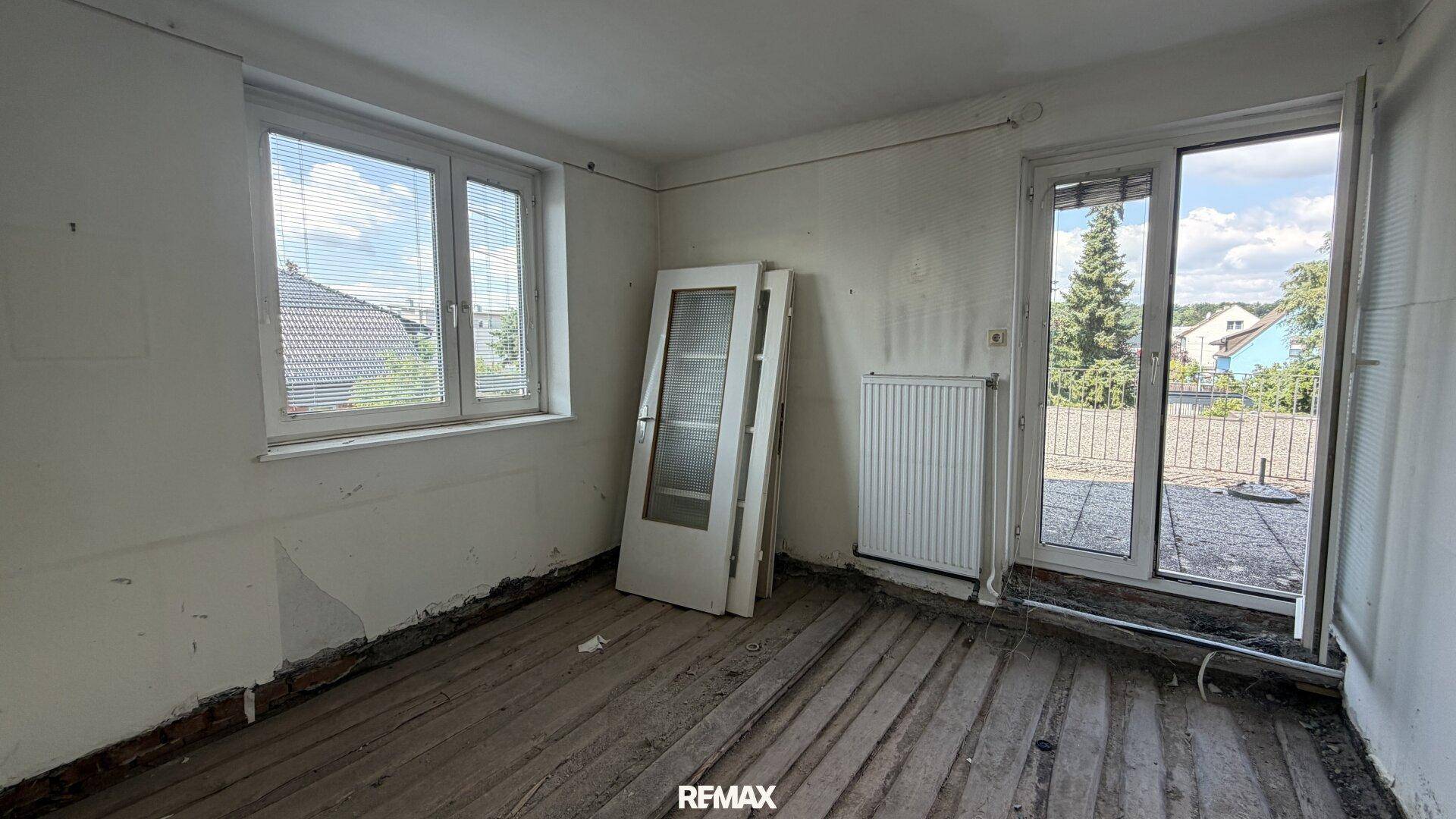 Raum im Rohbau mit zwei Fenstern und Balkonzugang, bereit für die Neugestaltung.