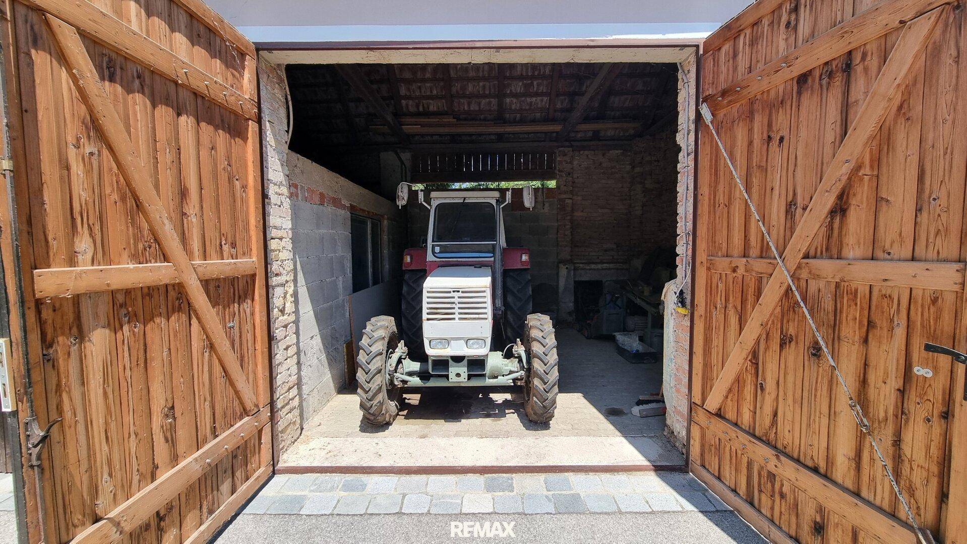 Große Scheune oder Garage mit Holztoren und einem geparkten Traktor im Inneren.