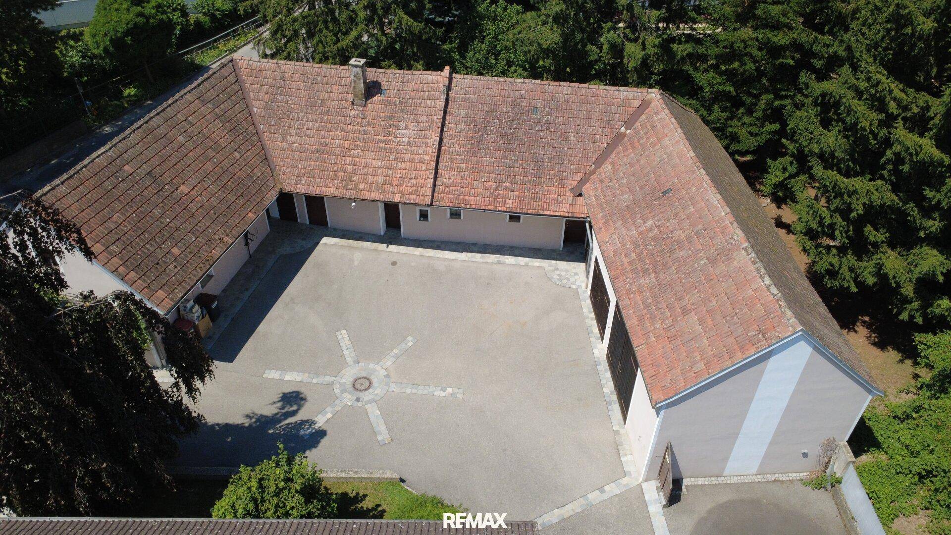 Luftaufnahme des weitläufigen Anwesens mit Innenhof und mehreren Gebäudeteilen unter blauem Himmel.