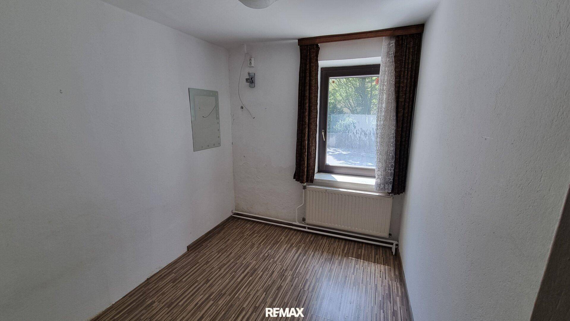 Helles Schlafzimmer mit Laminatboden und einem Fenster mit Blick ins Grüne.