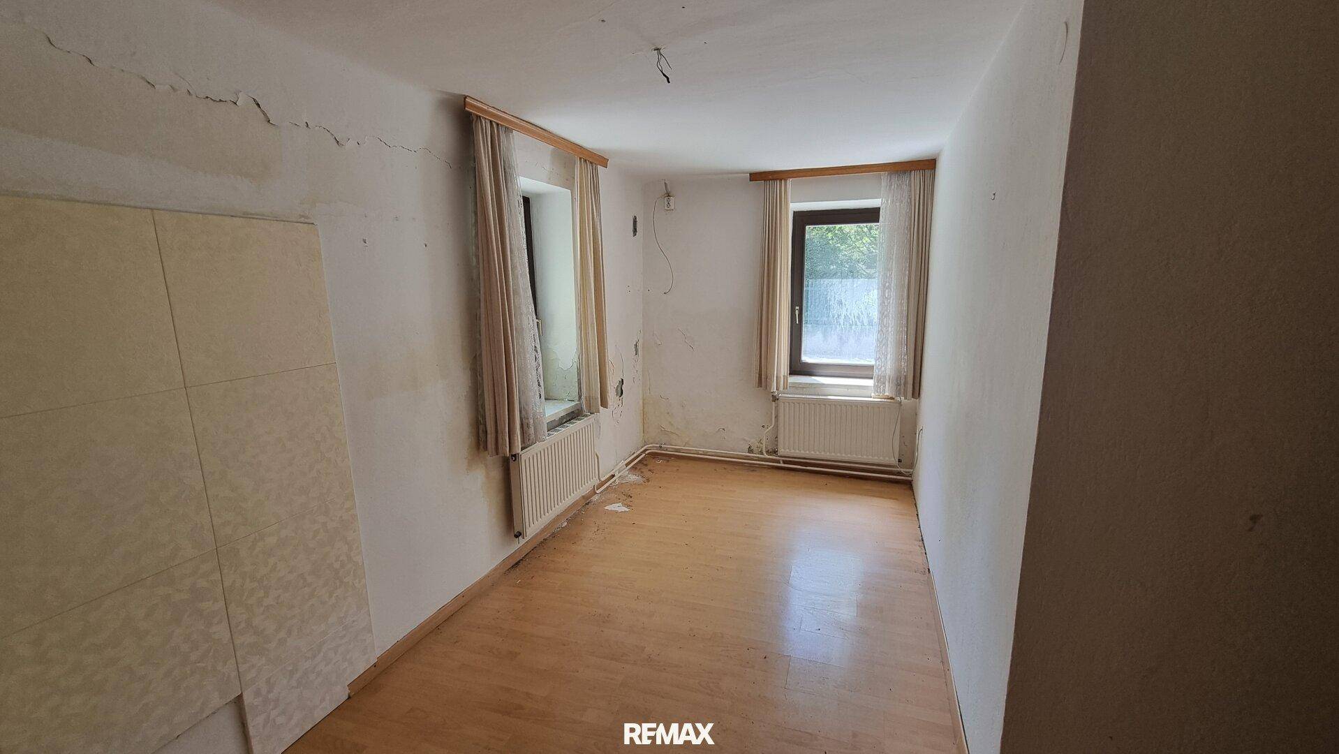 Renovierungsbedürftiger Raum mit Holzboden und zwei Fenstern, die viel Licht hereinlassen.