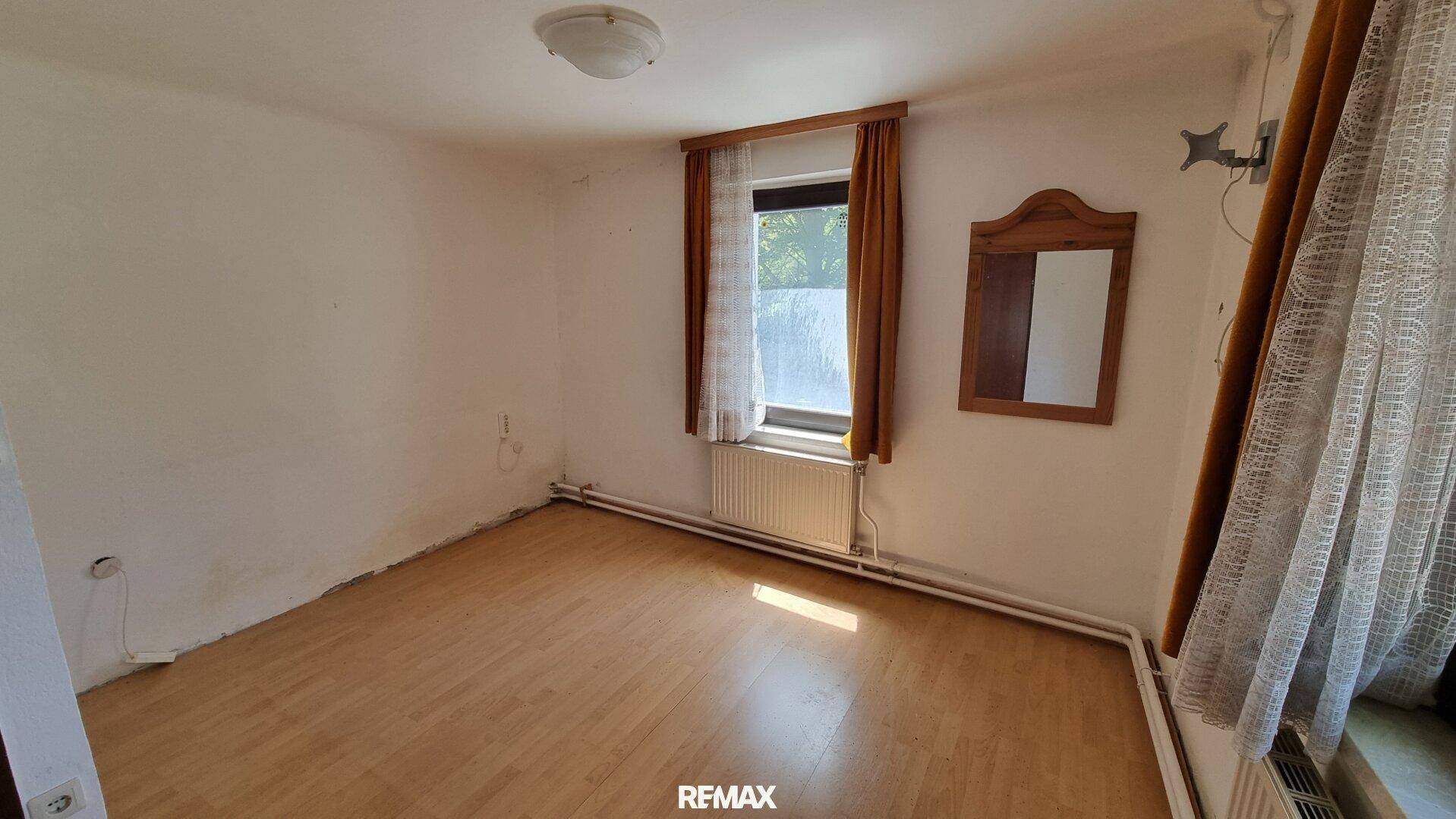 Helles Schlafzimmer mit Holzboden, Fenster und einem Spiegel an der Wand.