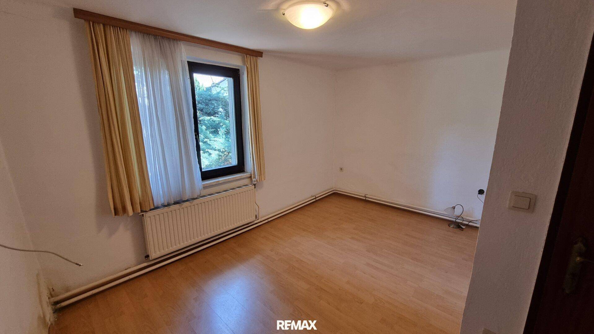 Helles Schlafzimmer mit Holzboden und einem Fenster mit Blick ins Grüne.
