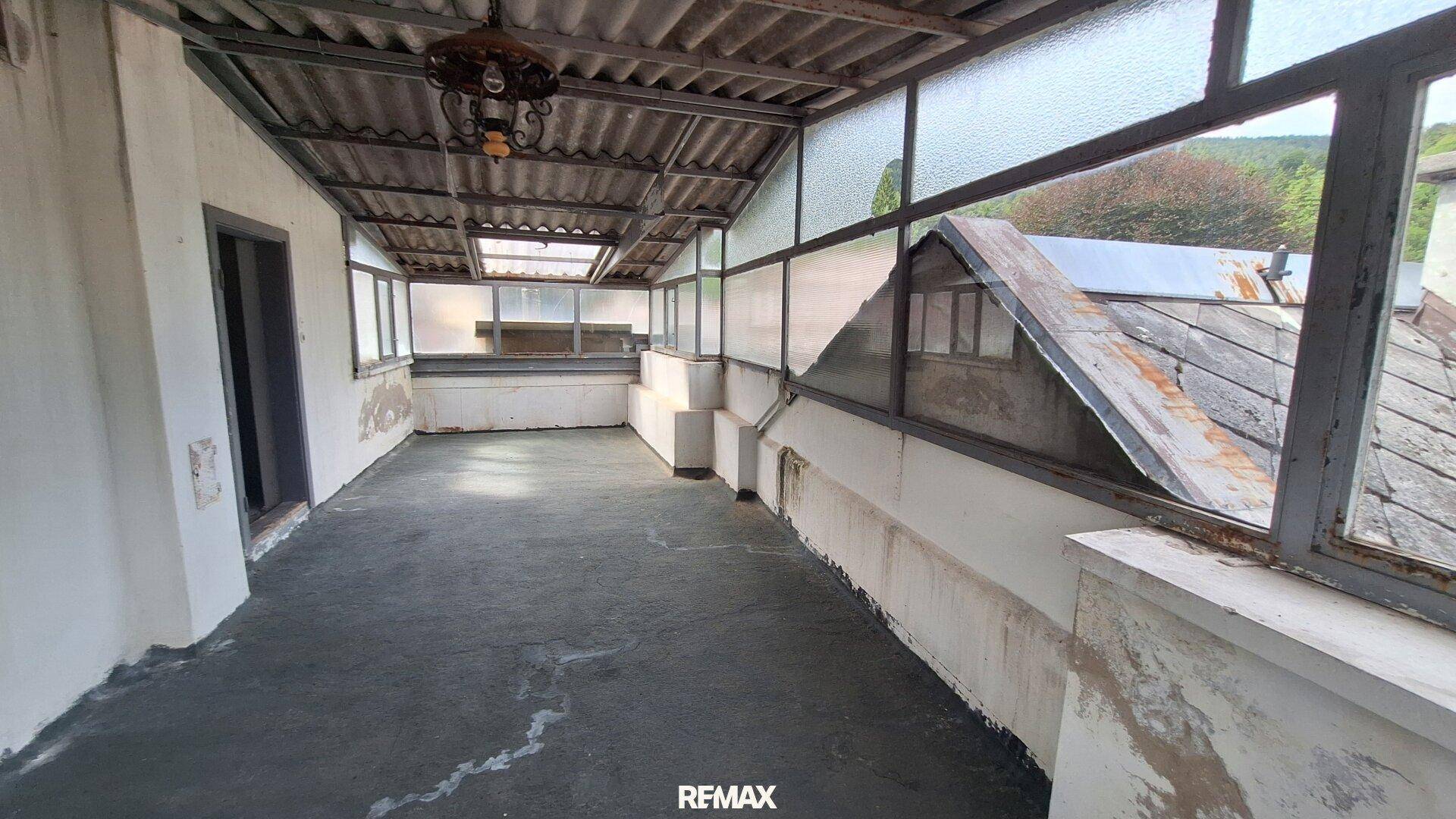 Überdachte Loggia mit Blick ins Grüne, in einem Zustand, der eine Renovierung erfordert.