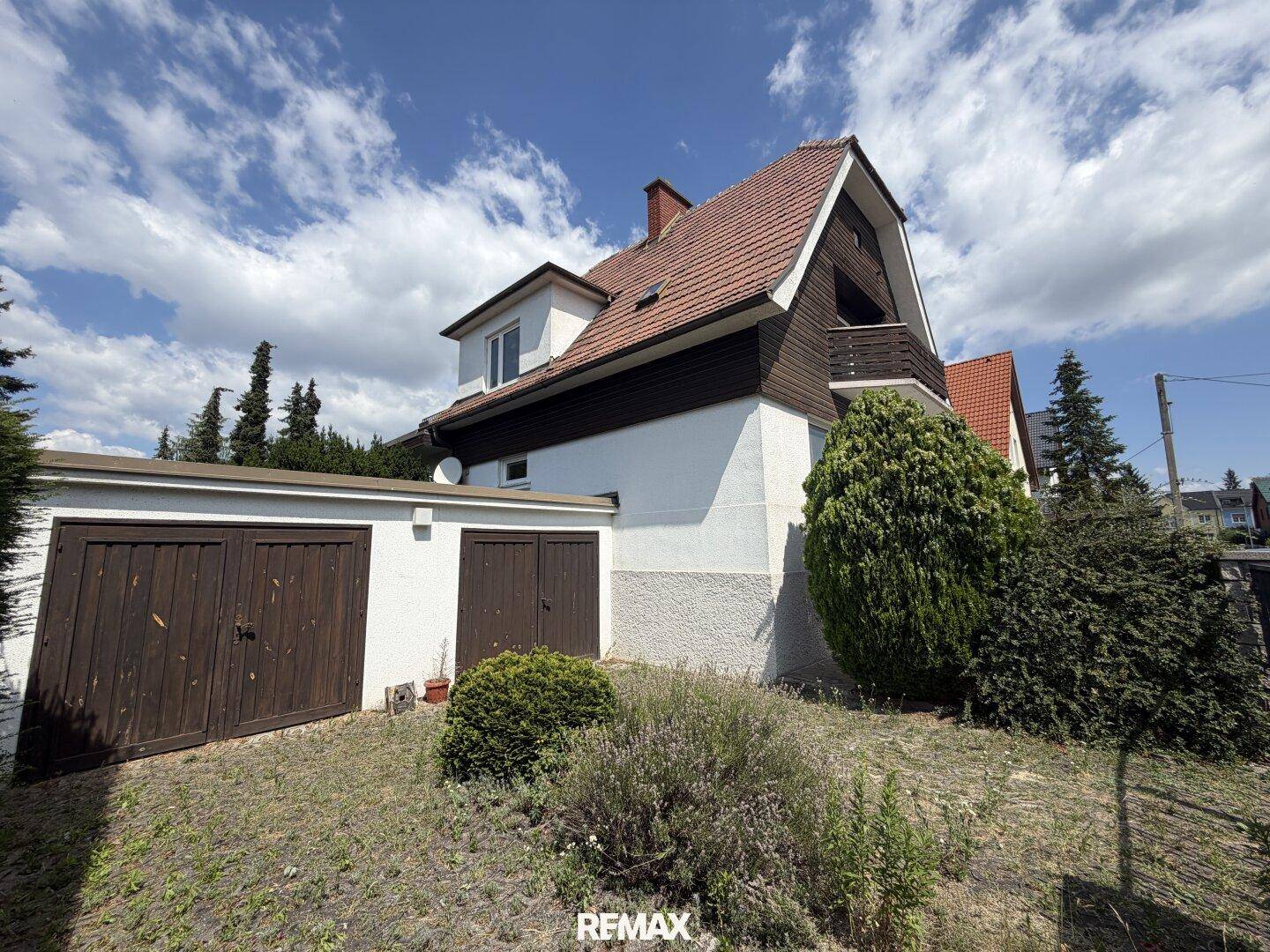 Doppelgarage neben dem Haus mit Satteldach und umgebender Bepflanzung.
