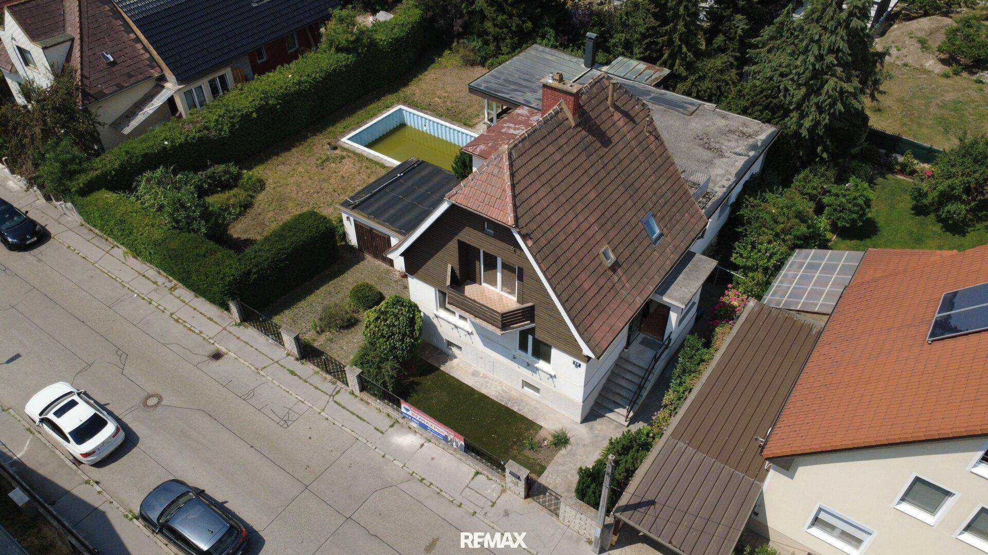 Luftaufnahme des Hauses mit Garten, Pool und angrenzenden Straßen und Nachbargebäuden.