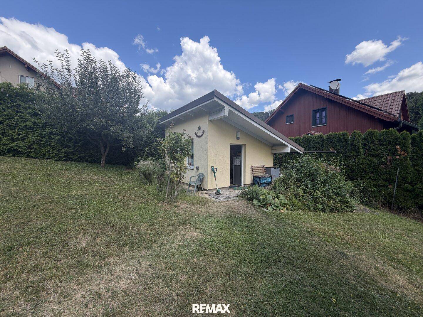 Kleines Nebengebäude auf einem grünen Hang mit umgebender Vegetation.