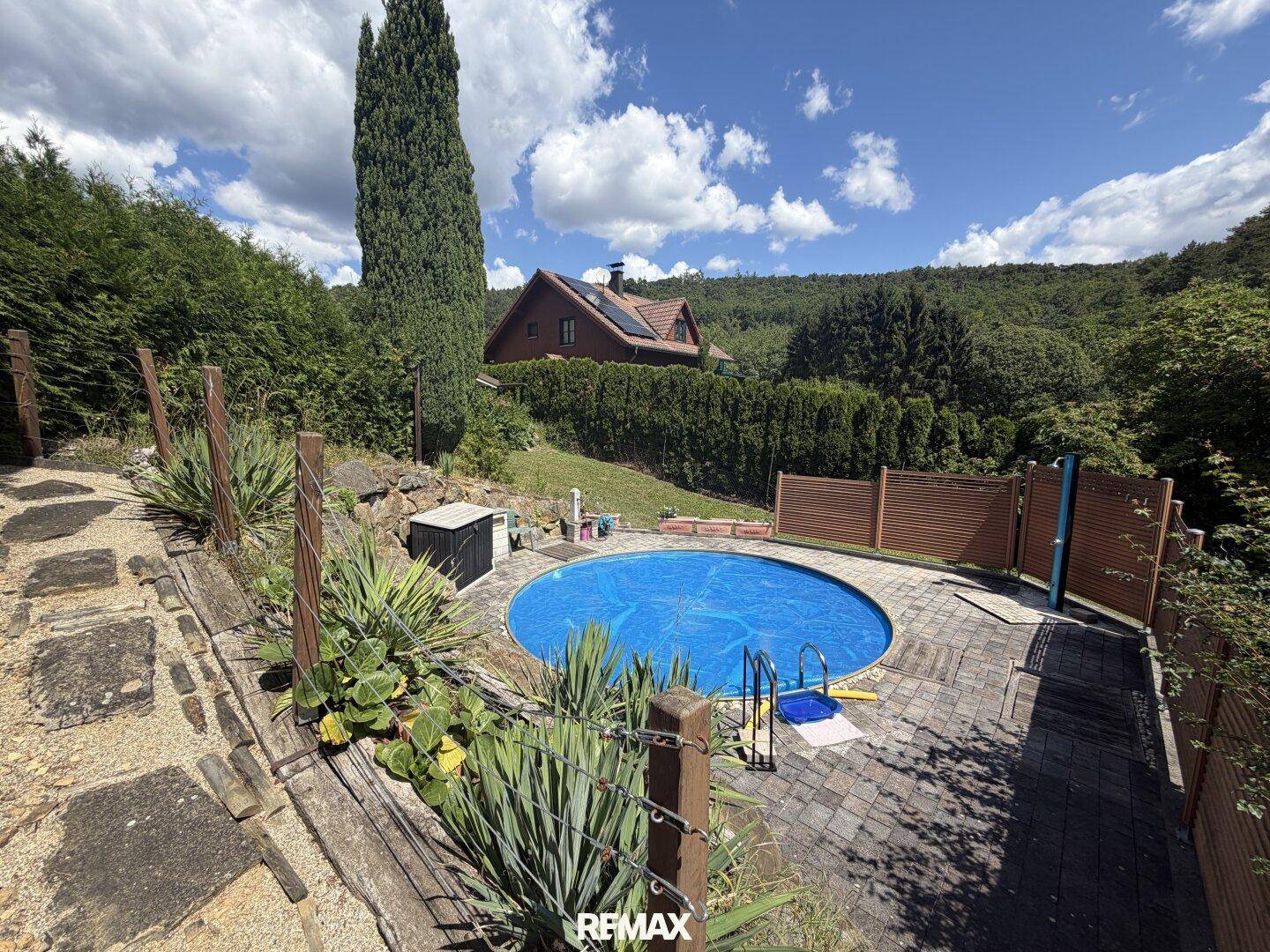 Runder Poolbereich mit gepflasterter Terrasse und Blick auf die bewaldete Umgebung.