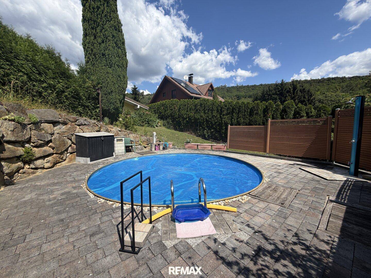 Runder Swimmingpool mit gepflasterter Umrandung und Treppe, umgeben von Naturstein.